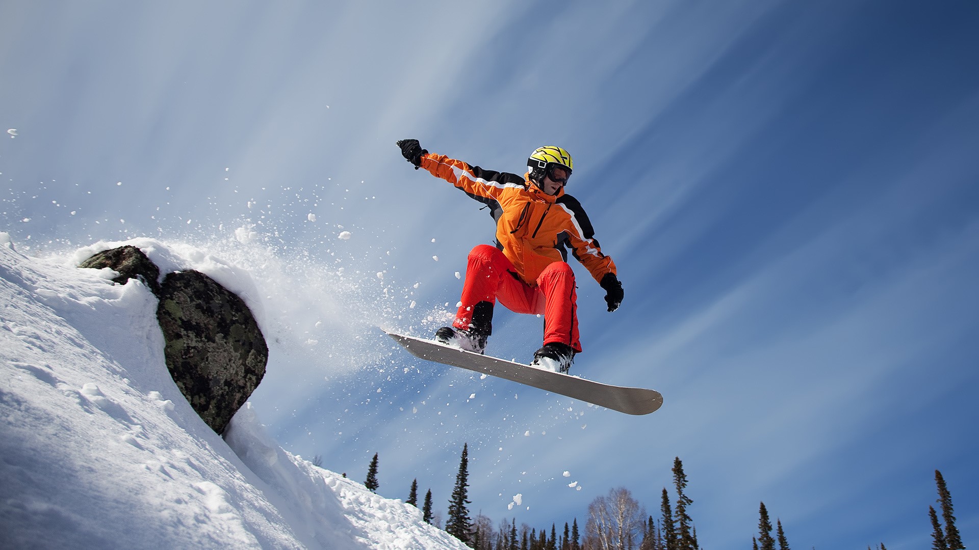 Snowboarder jumping off a snowy rock HD Wallpaper