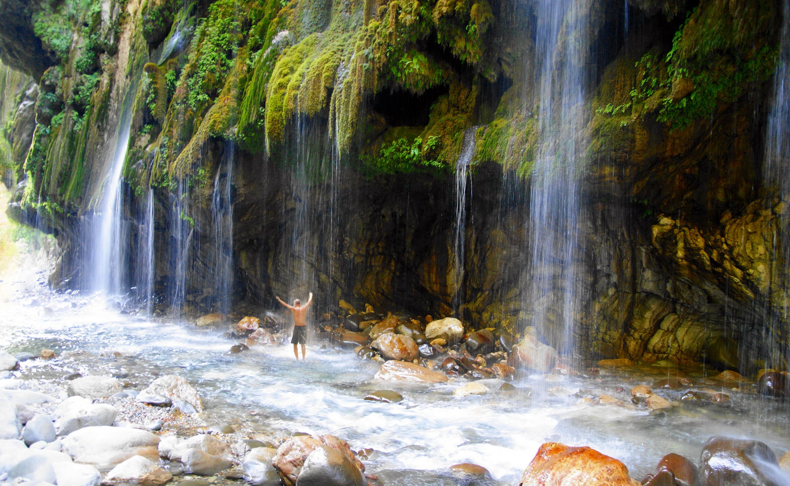 Man standing under waterfalls in a rocky gorge HD Wallpaper