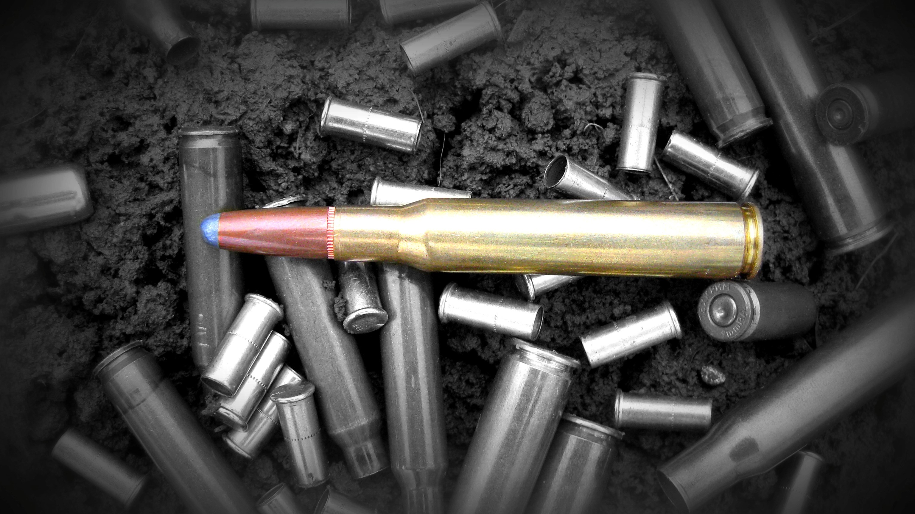 A single rifle cartridge surrounded by spent casings HD Wallpaper