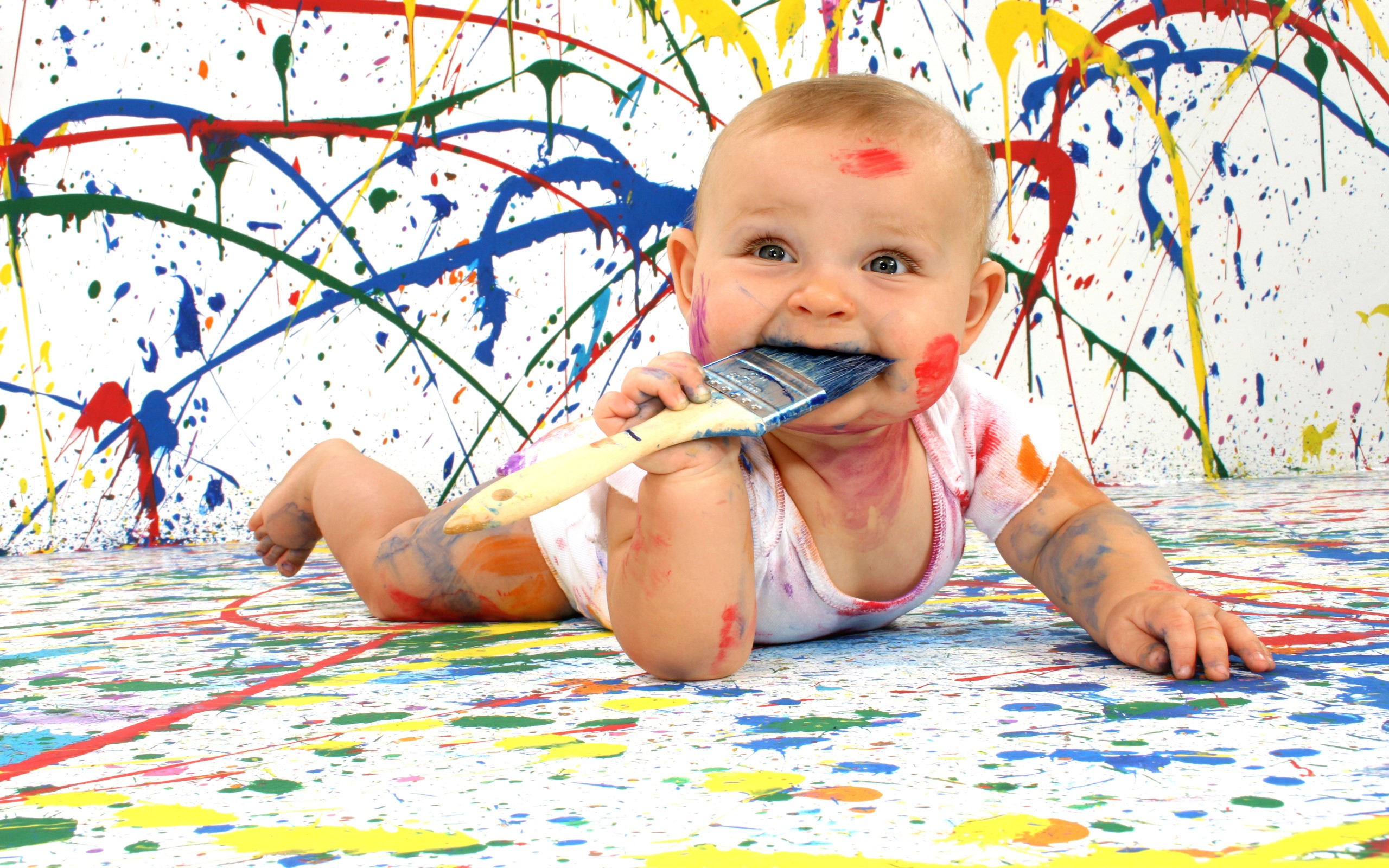 Baby covered in paint chewing on a paintbrush HD Wallpaper