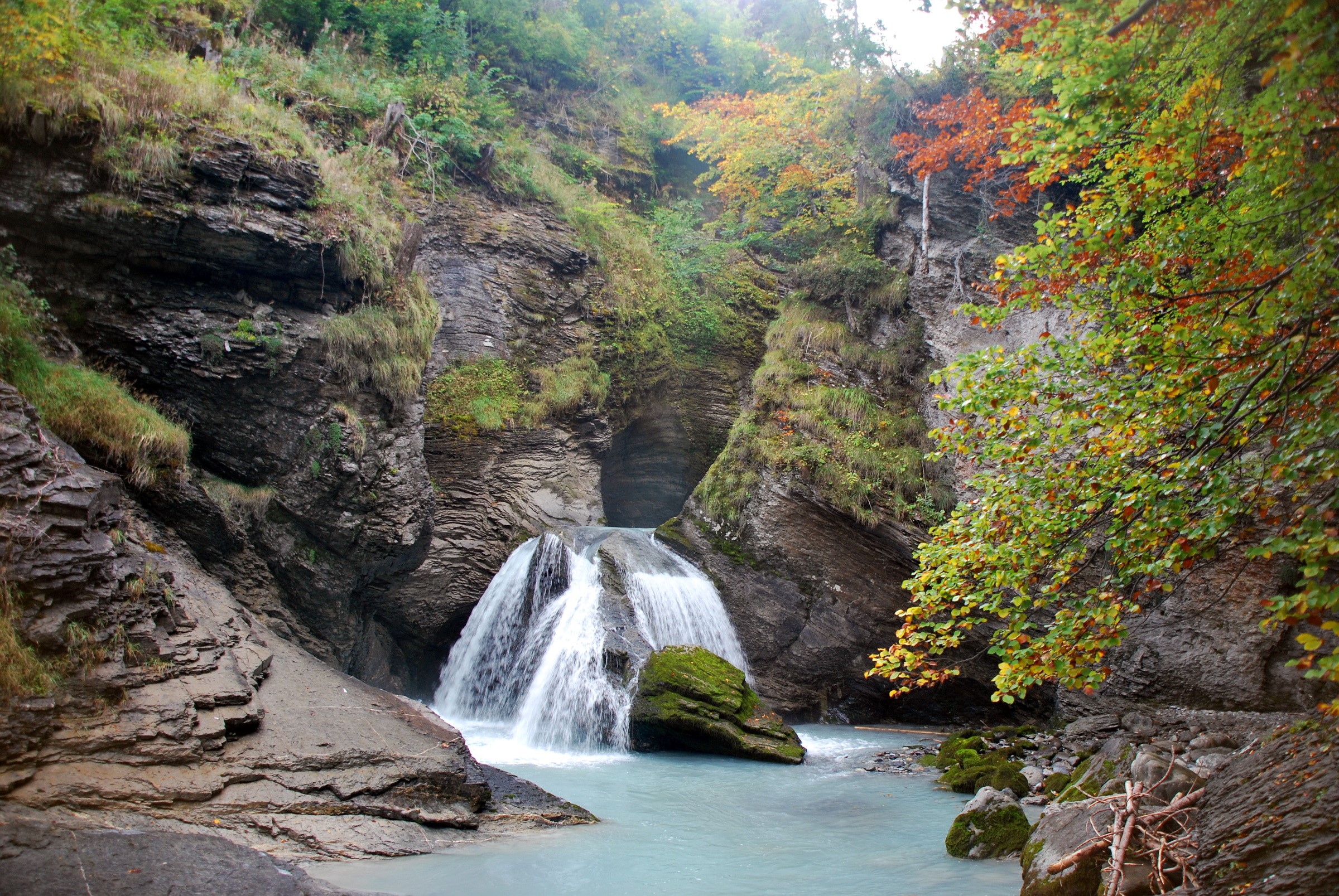 Waterfall cascading into a turquoise pool surrounded by rocks and trees HD Wallpaper
