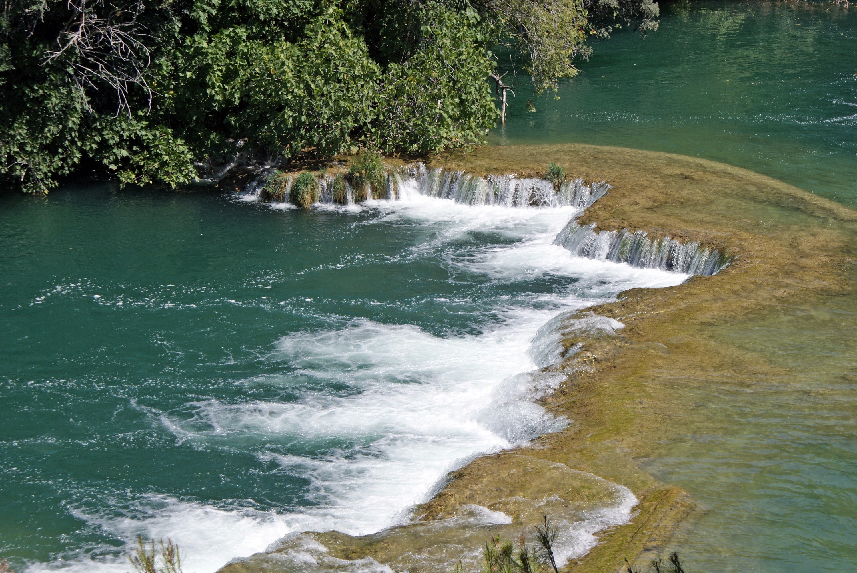 Waterfalls and lush green trees by a river HD Wallpaper