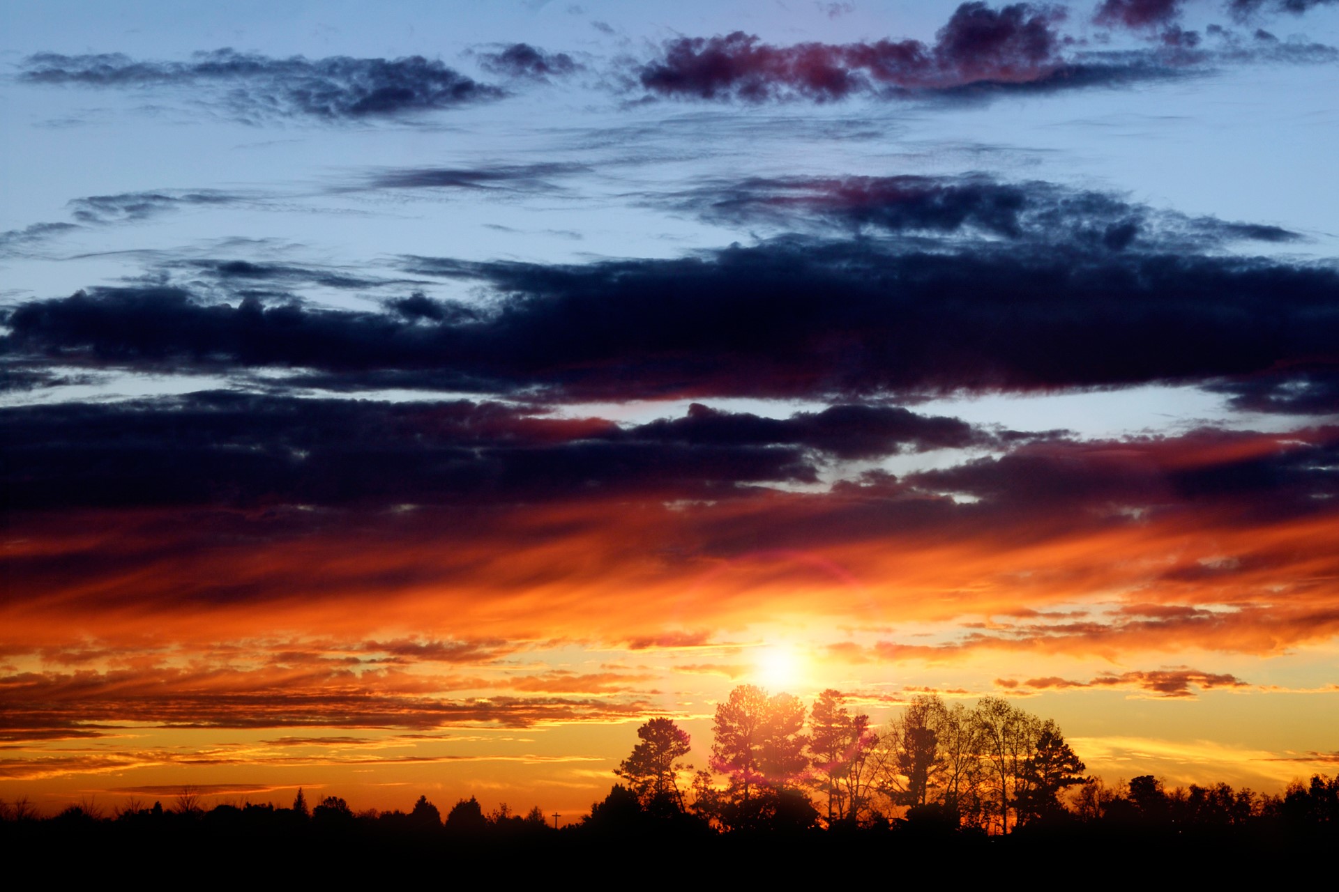 Sunset with dramatic clouds over silhouetted trees HD Wallpaper