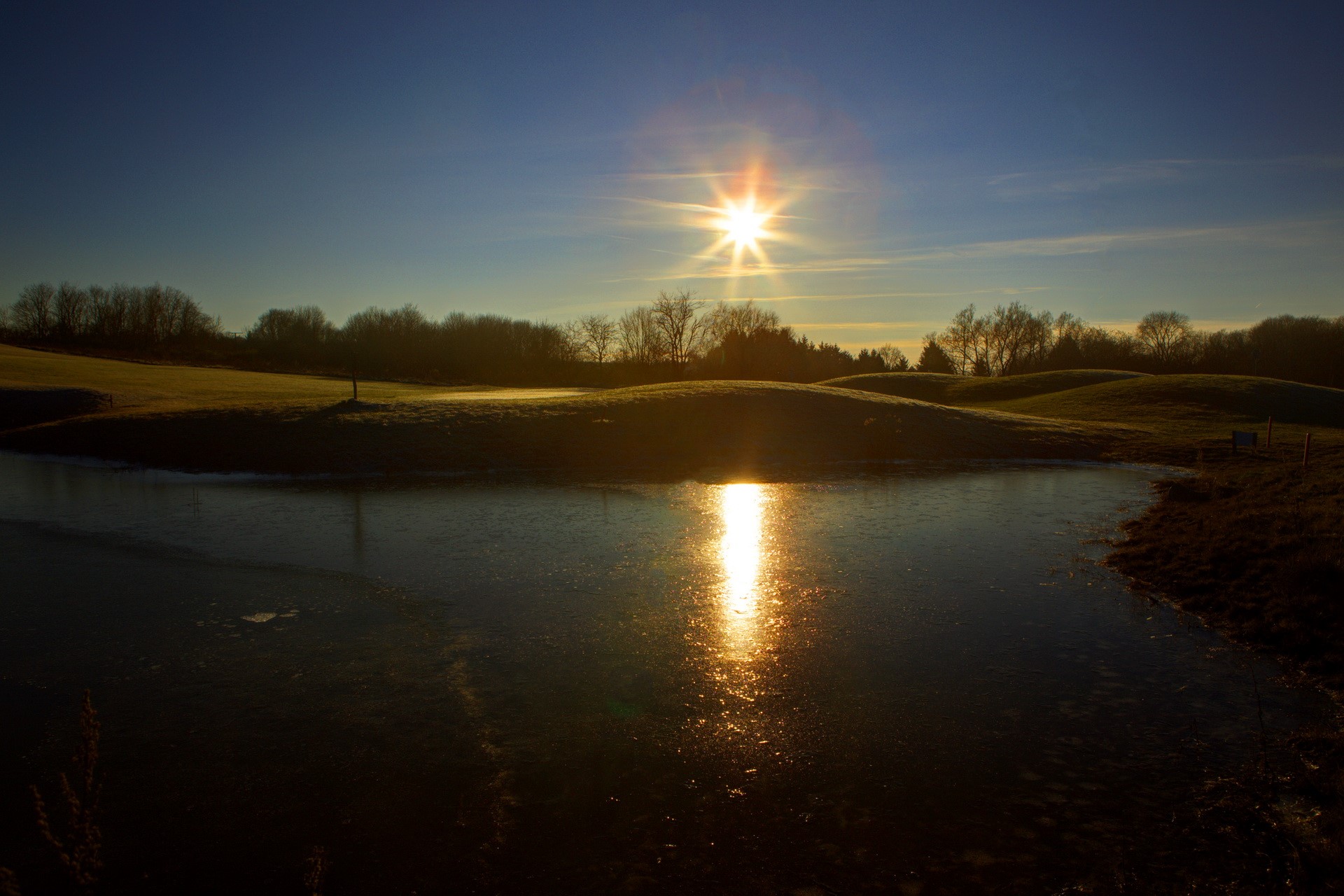 Sun reflecting on frozen pond with golf course background HD Wallpaper