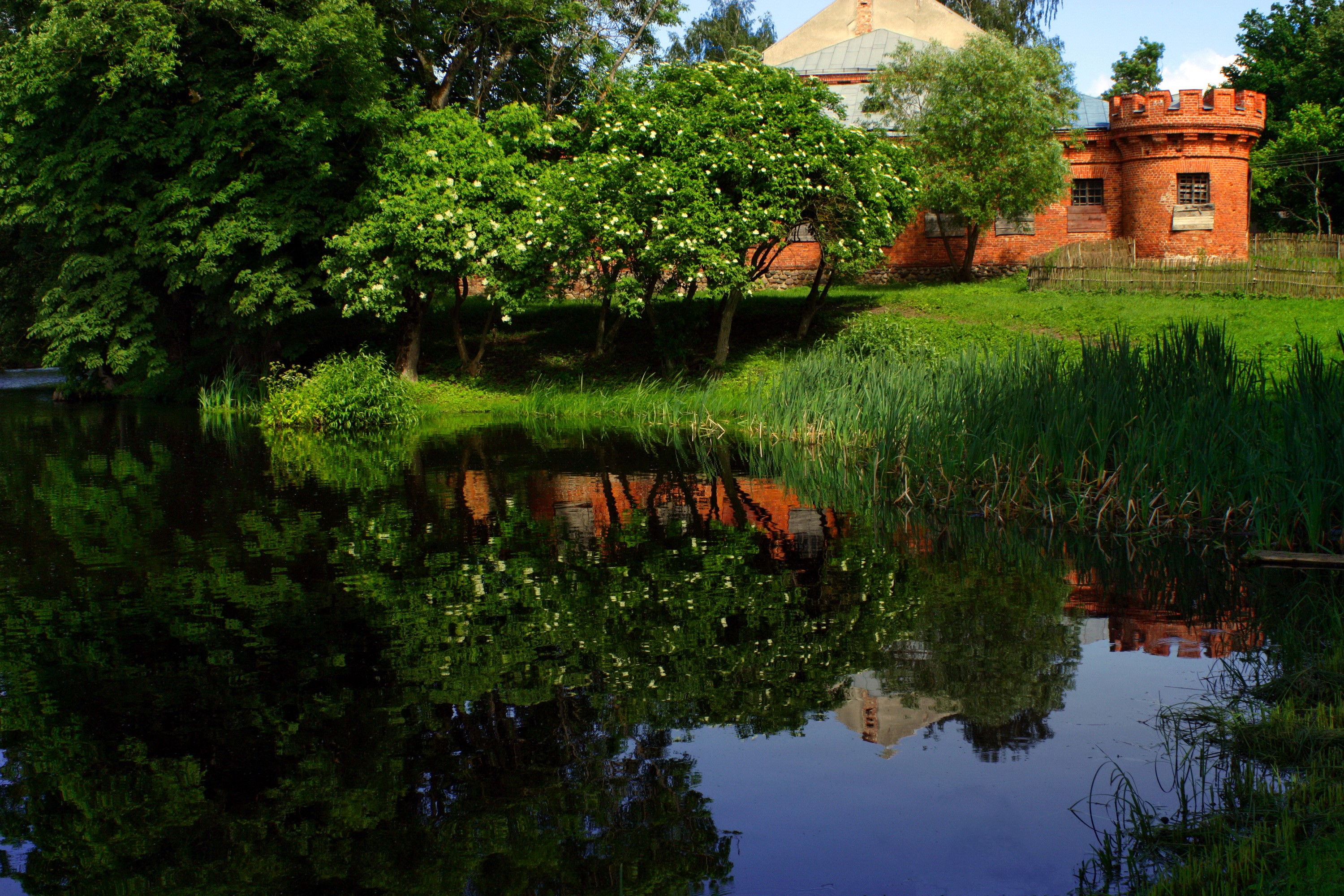 Brick tower reflected in a calm river surrounded by trees HD Wallpaper