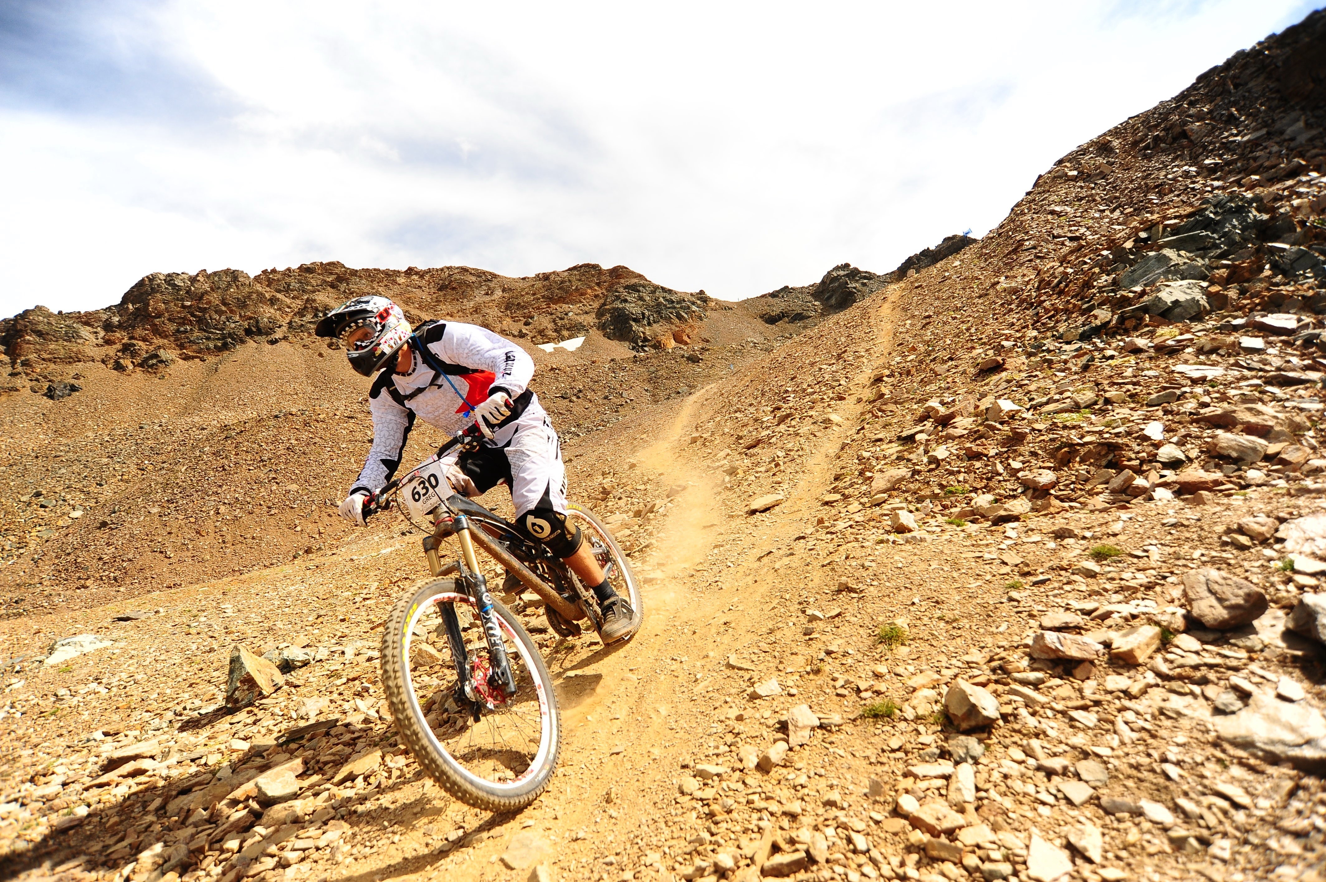 Mountain biker racing downhill on a rocky slope HD Wallpaper