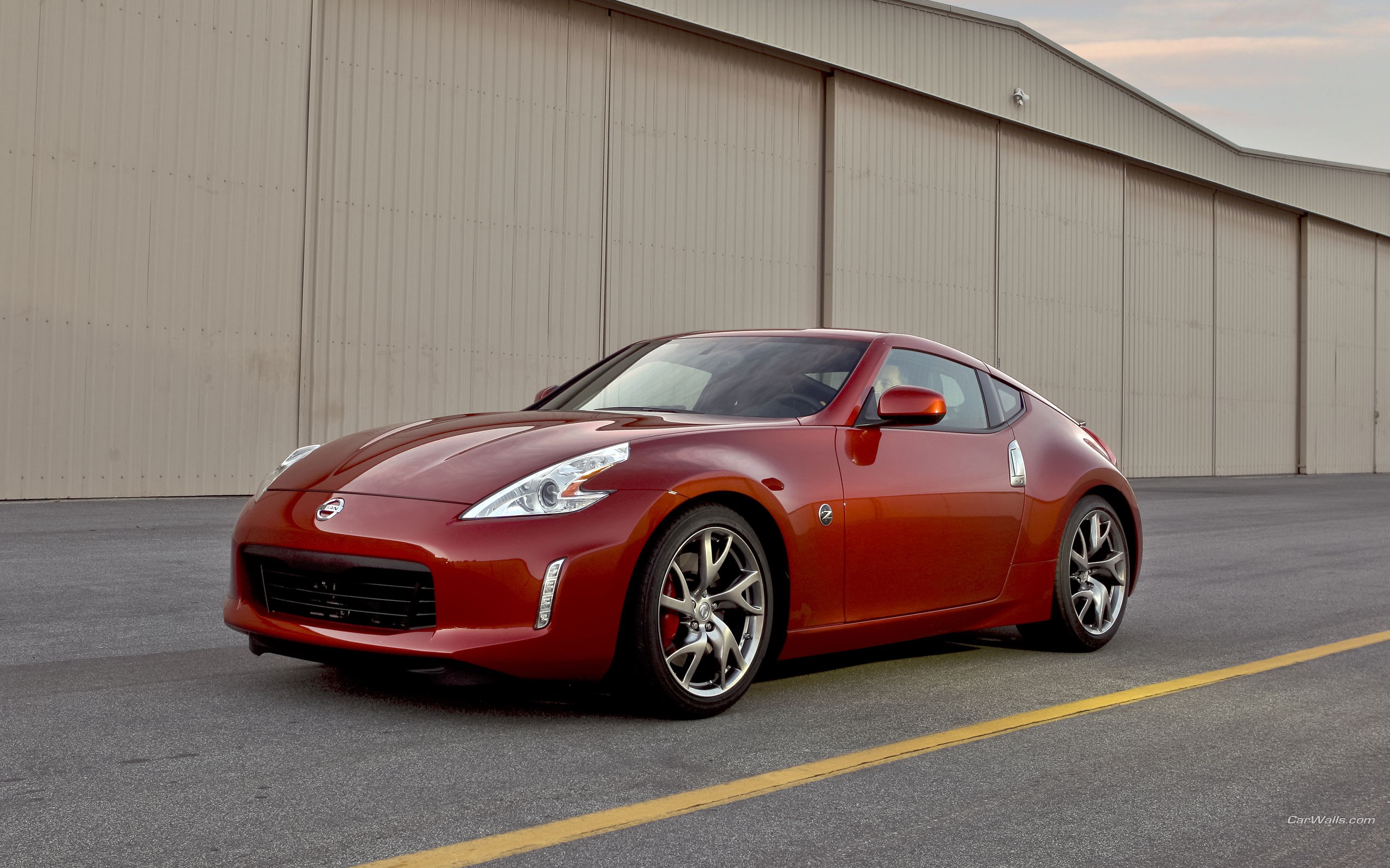 Red Nissan 370Z parked in front of a hangar HD Wallpaper