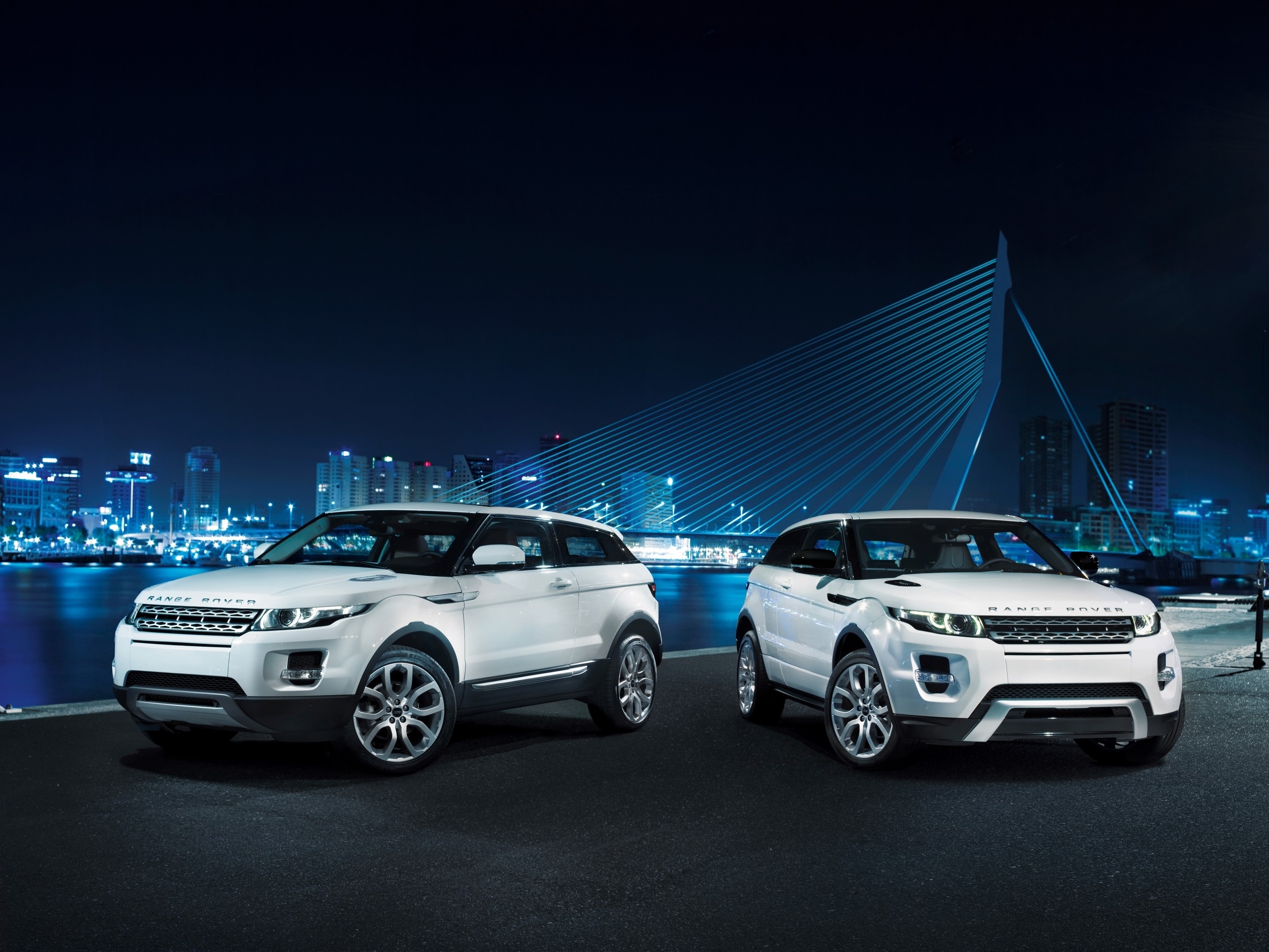 Two white Range Rover Evoque SUVs at night with city and bridge in background HD Wallpaper