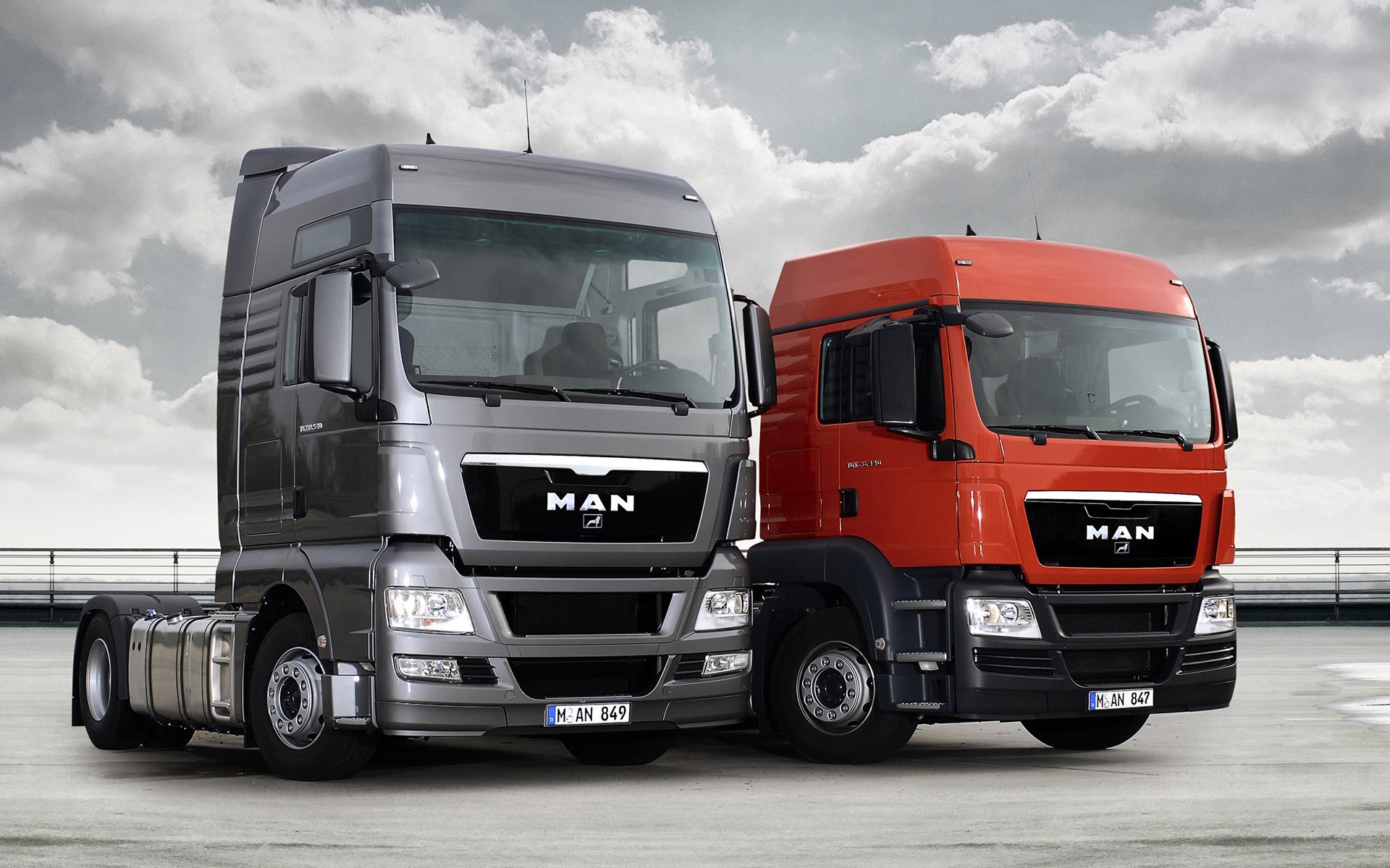 Two MAN SE trucks, one gray and one orange HD Wallpaper