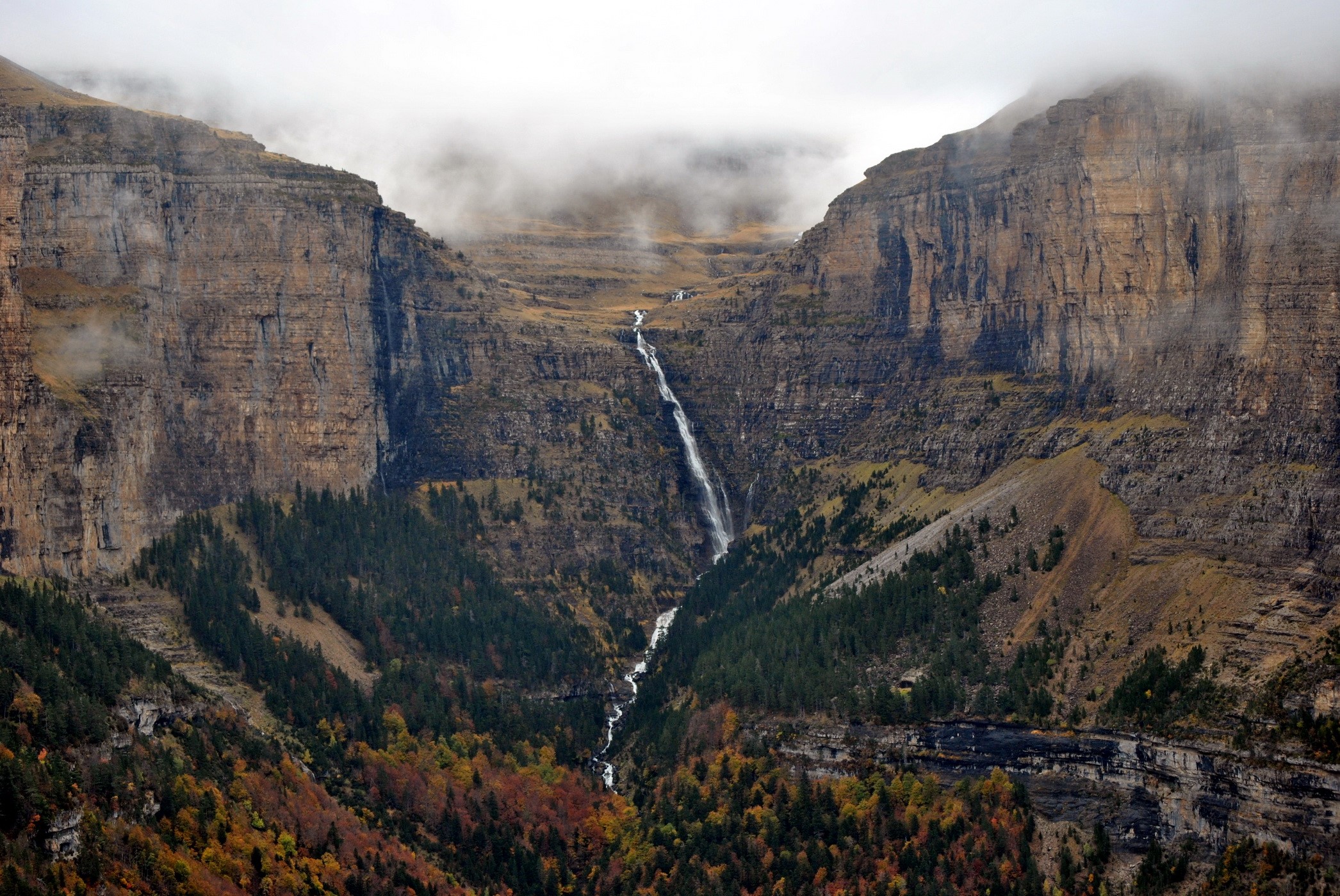 Waterfall cascading down a rocky mountain valley with autumn trees HD Wallpaper