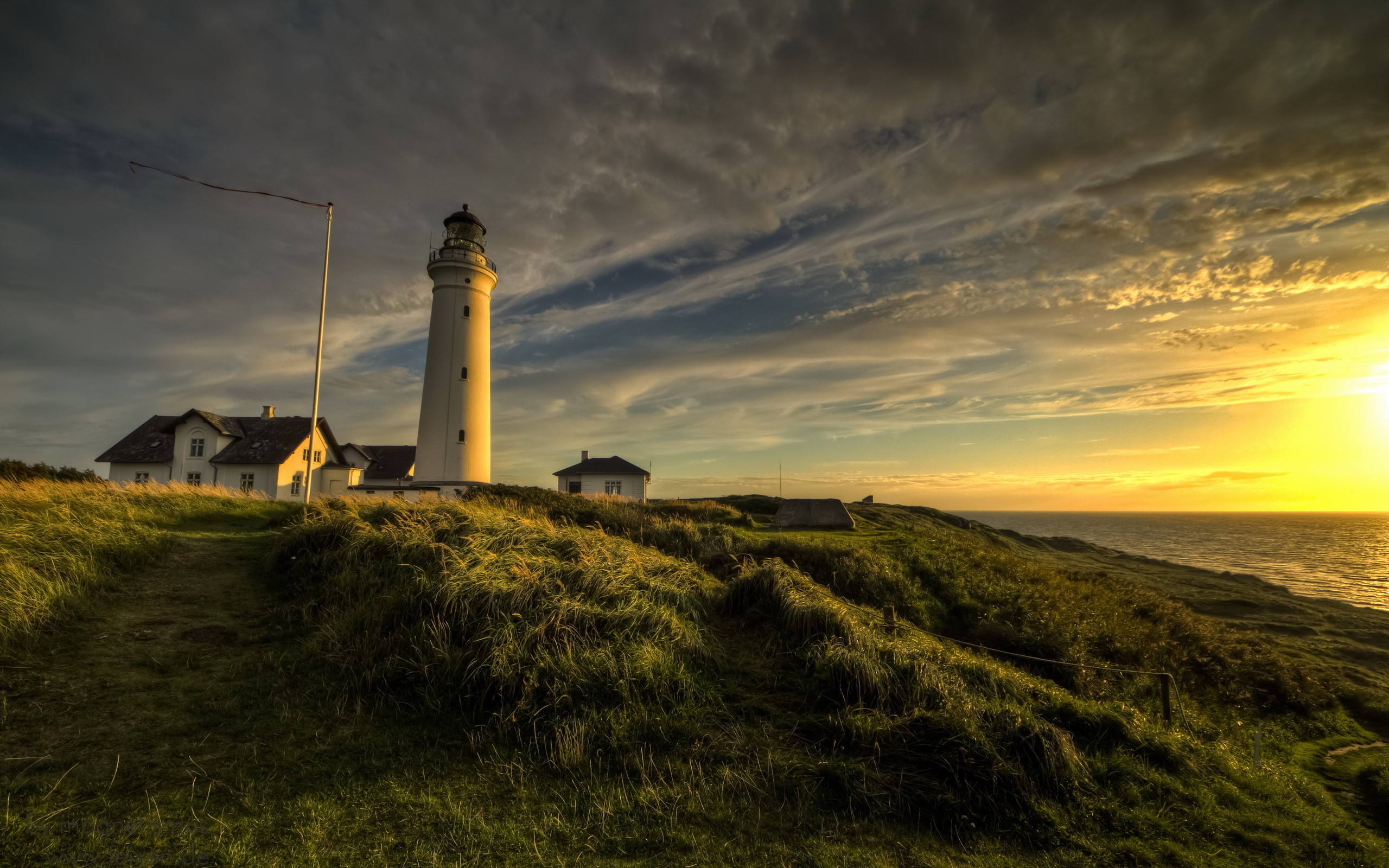 Lighthouse on a grassy coast at sunset HD Wallpaper