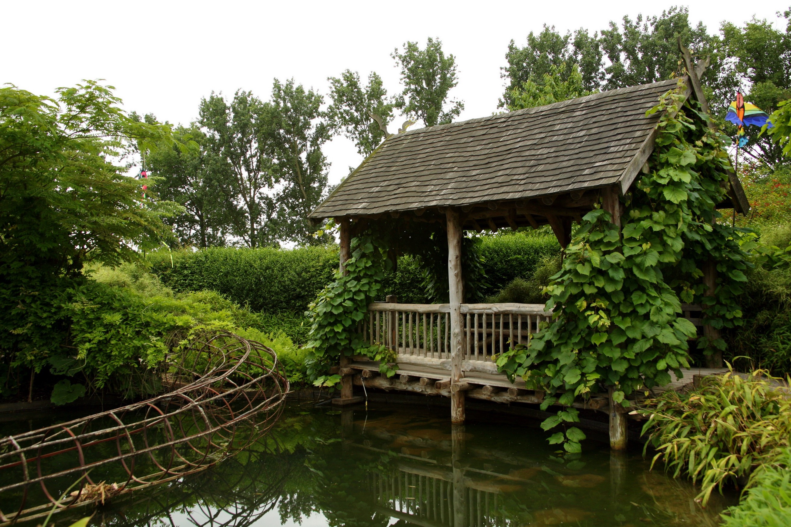 Wooden gazebo by a pond with overgrown vines HD Wallpaper