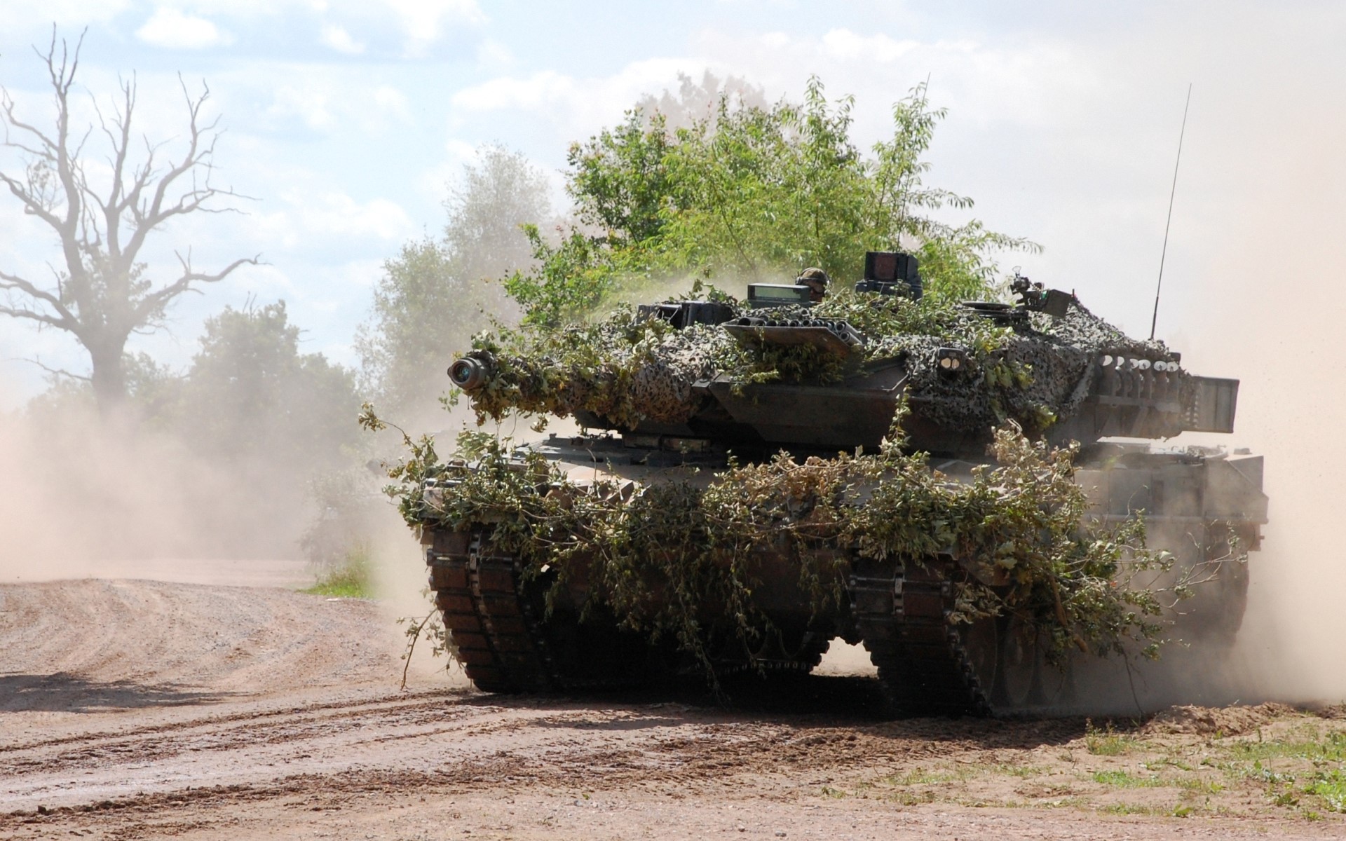 Camouflaged tank driving on a dirt road HD Wallpaper