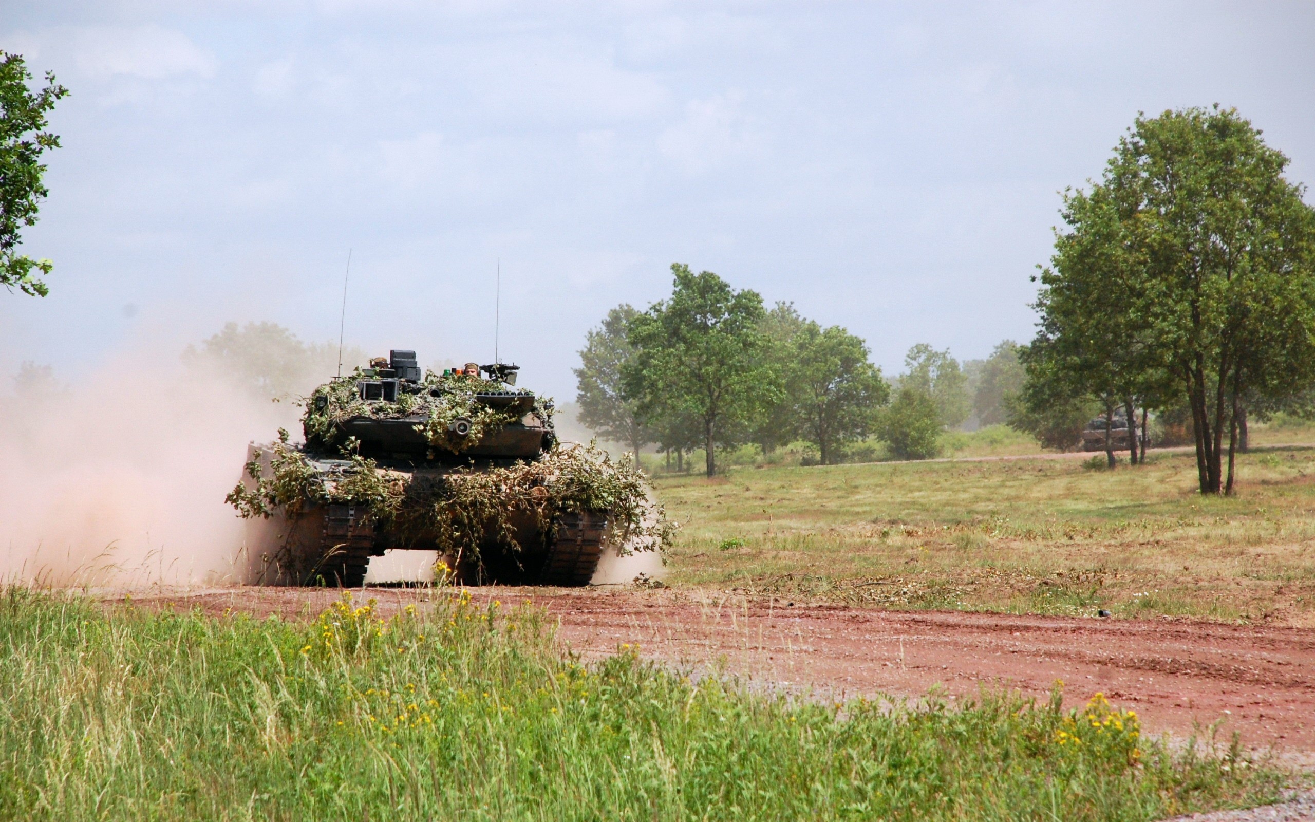 Camouflaged tank kicking up dust on a dirt road HD Wallpaper
