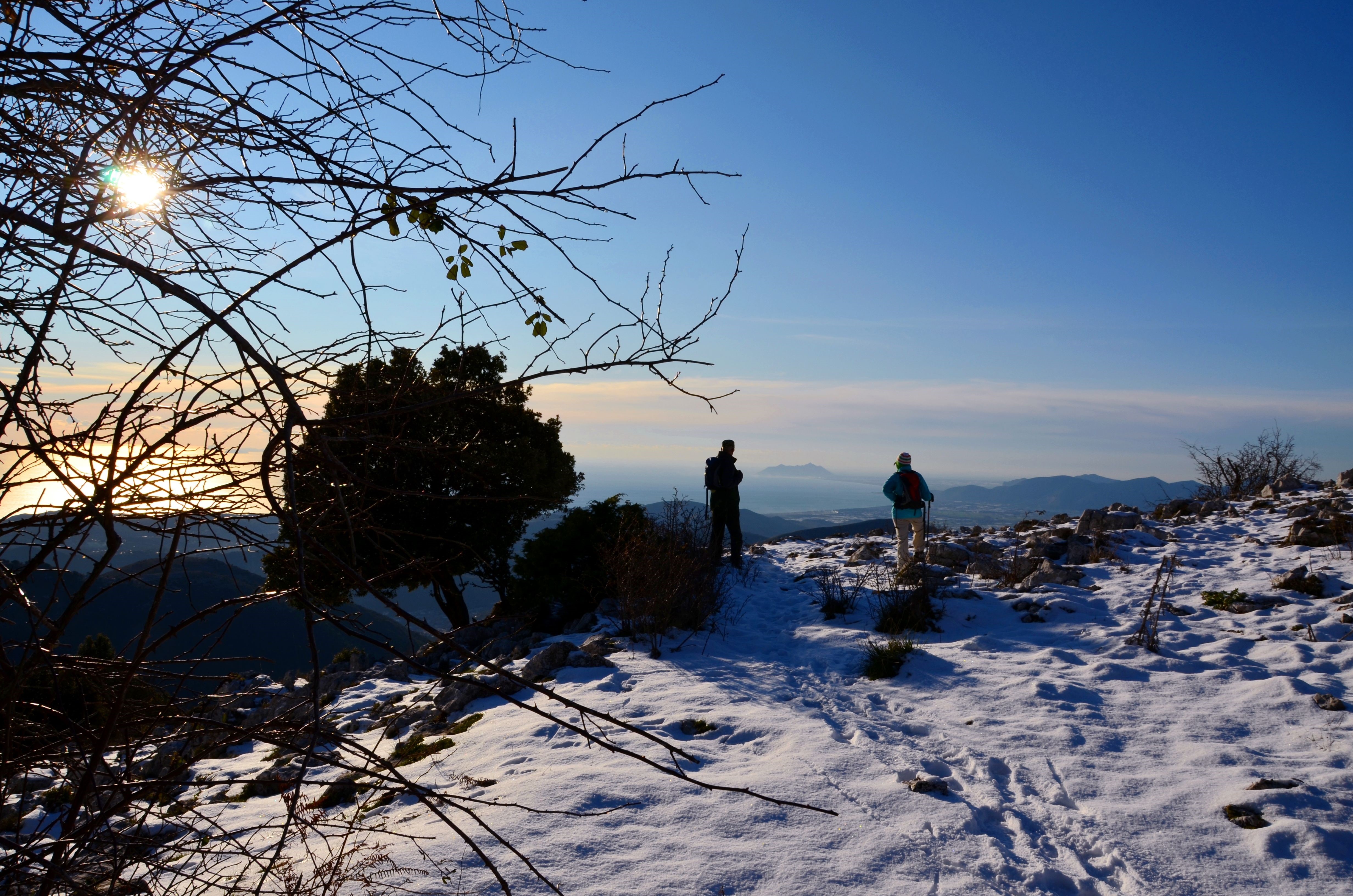 Two hikers on a snowy mountain overlooking the sea HD Wallpaper