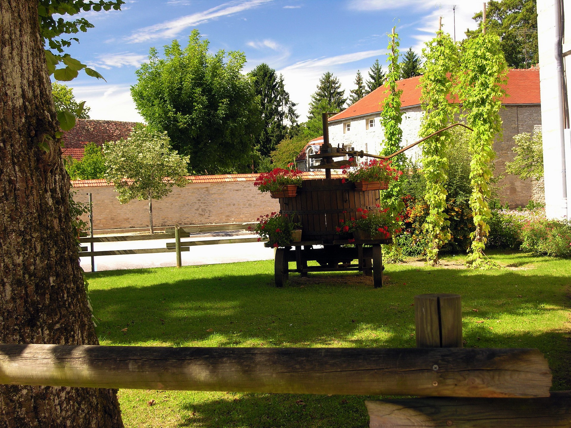 Wooden wine press with flowers in front of stone building HD Wallpaper