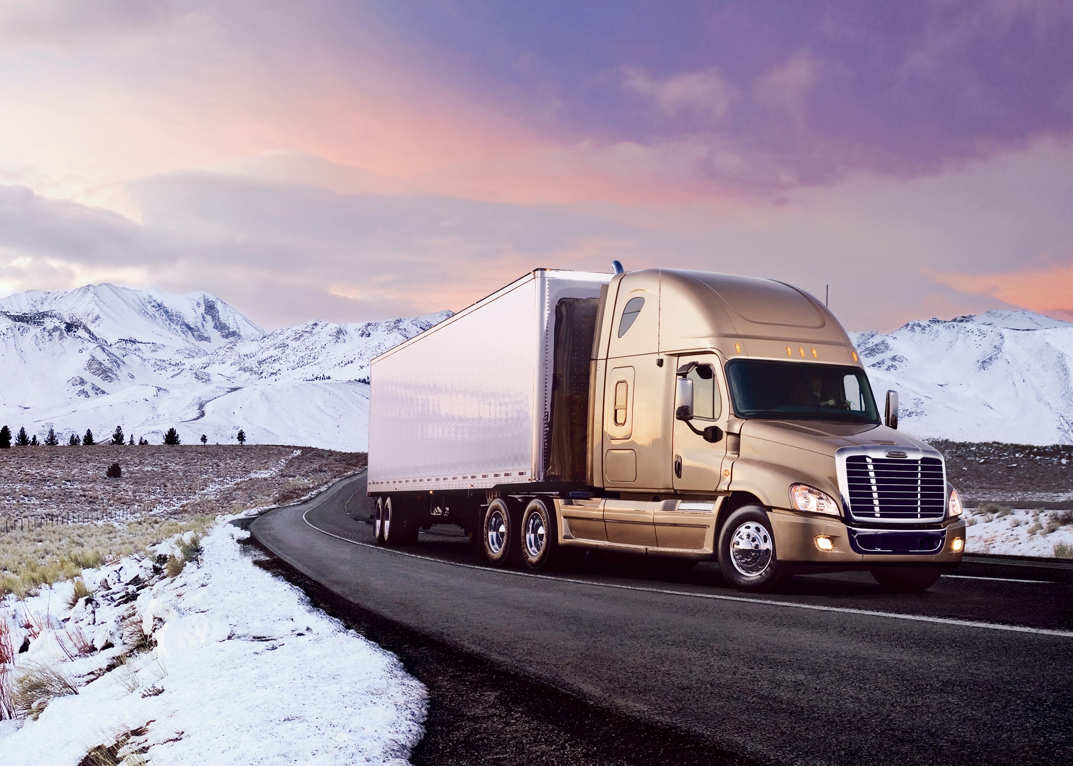 Freightliner semi-truck driving on a snowy mountain road HD Wallpaper