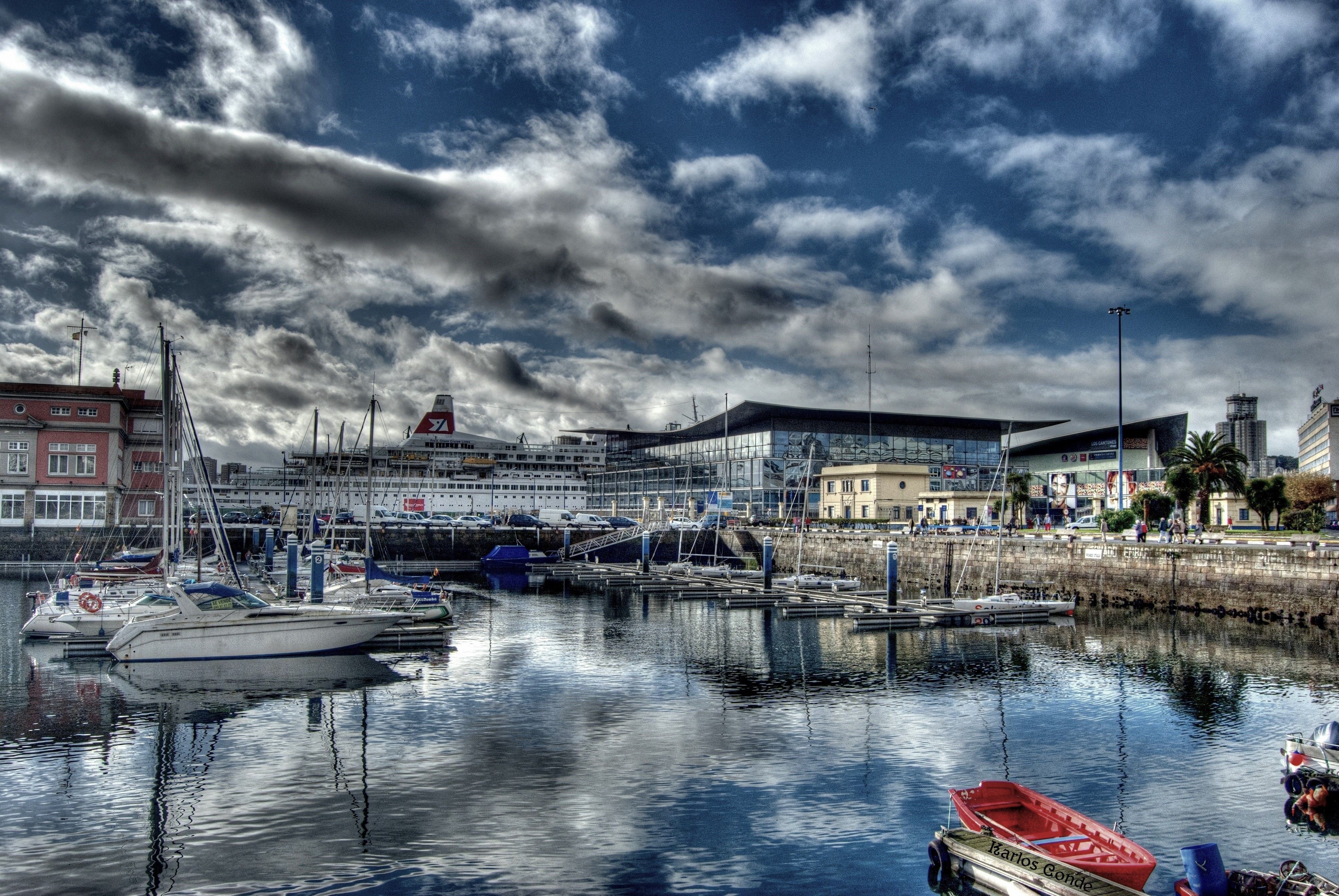 Boats docked in a harbor with a large ship and modern buildings in Spain HD Wallpaper