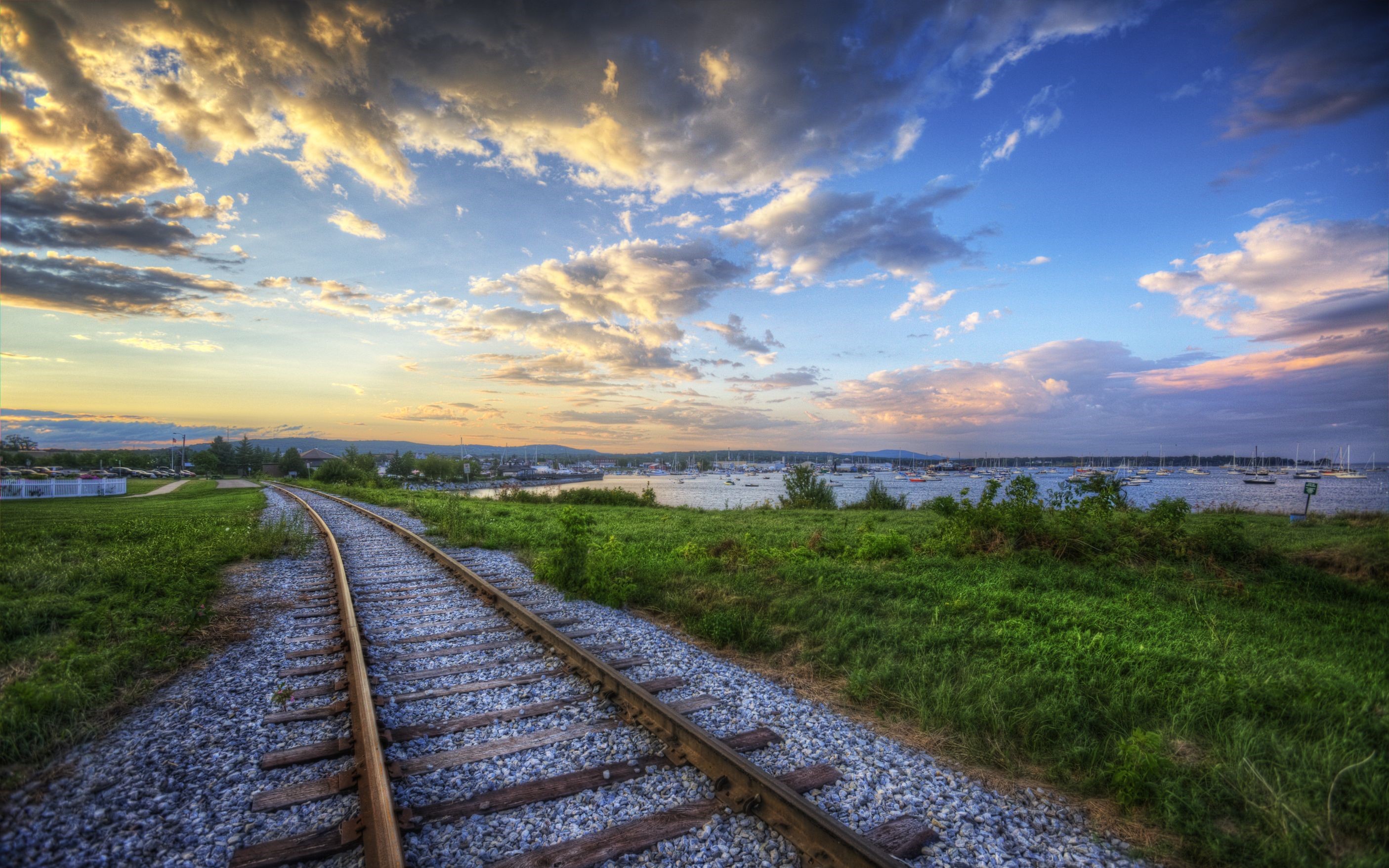 Railroad tracks leading to a harbor with sailboats at sunset HD Wallpaper