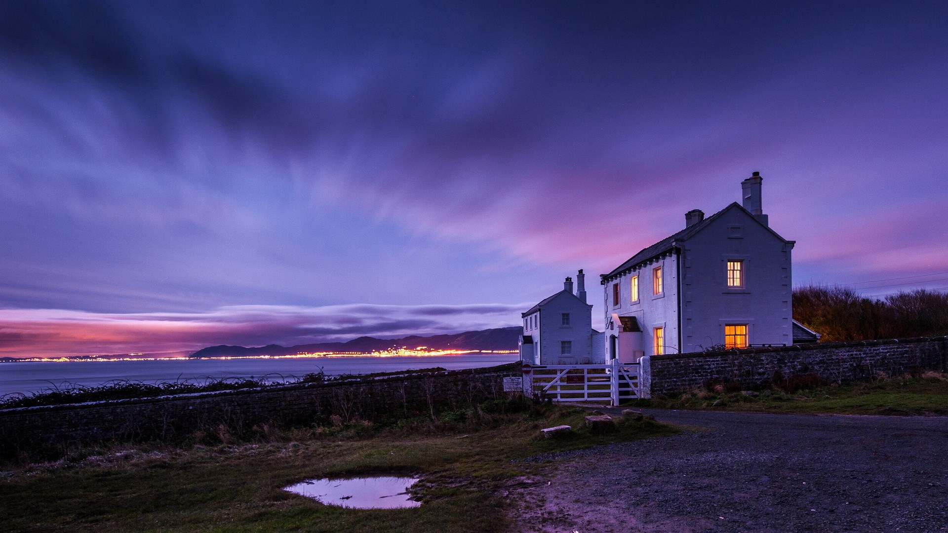 Coastal houses at twilight with distant city lights HD Wallpaper