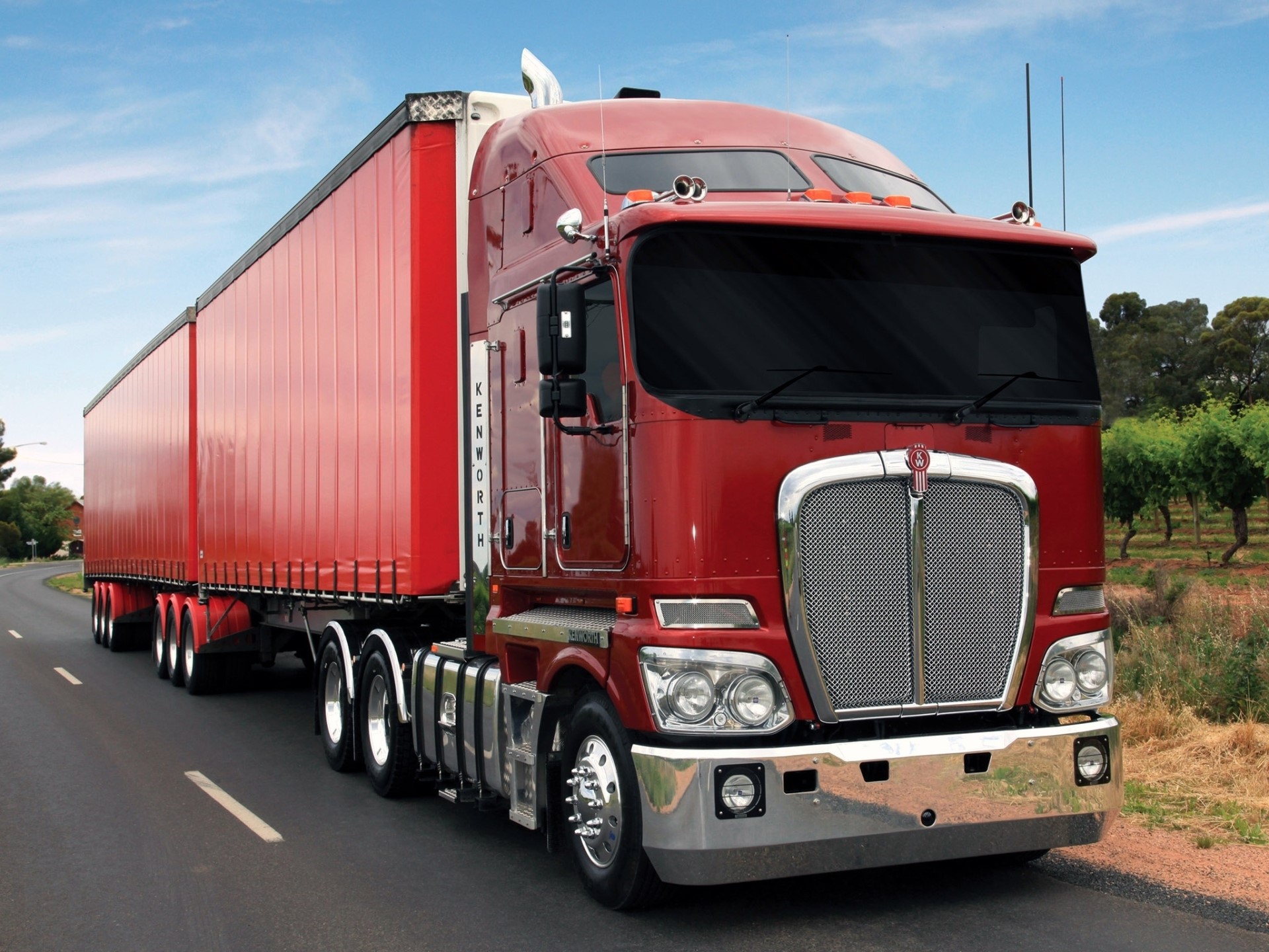 Red Kenworth semi-truck with trailer on road HD Wallpaper