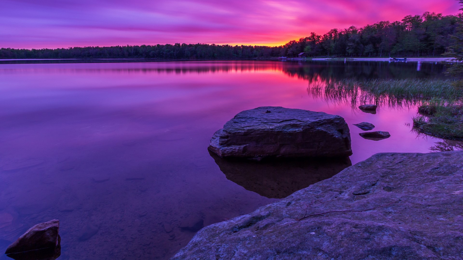 Purple sunset over a calm lake with rocks HD Wallpaper