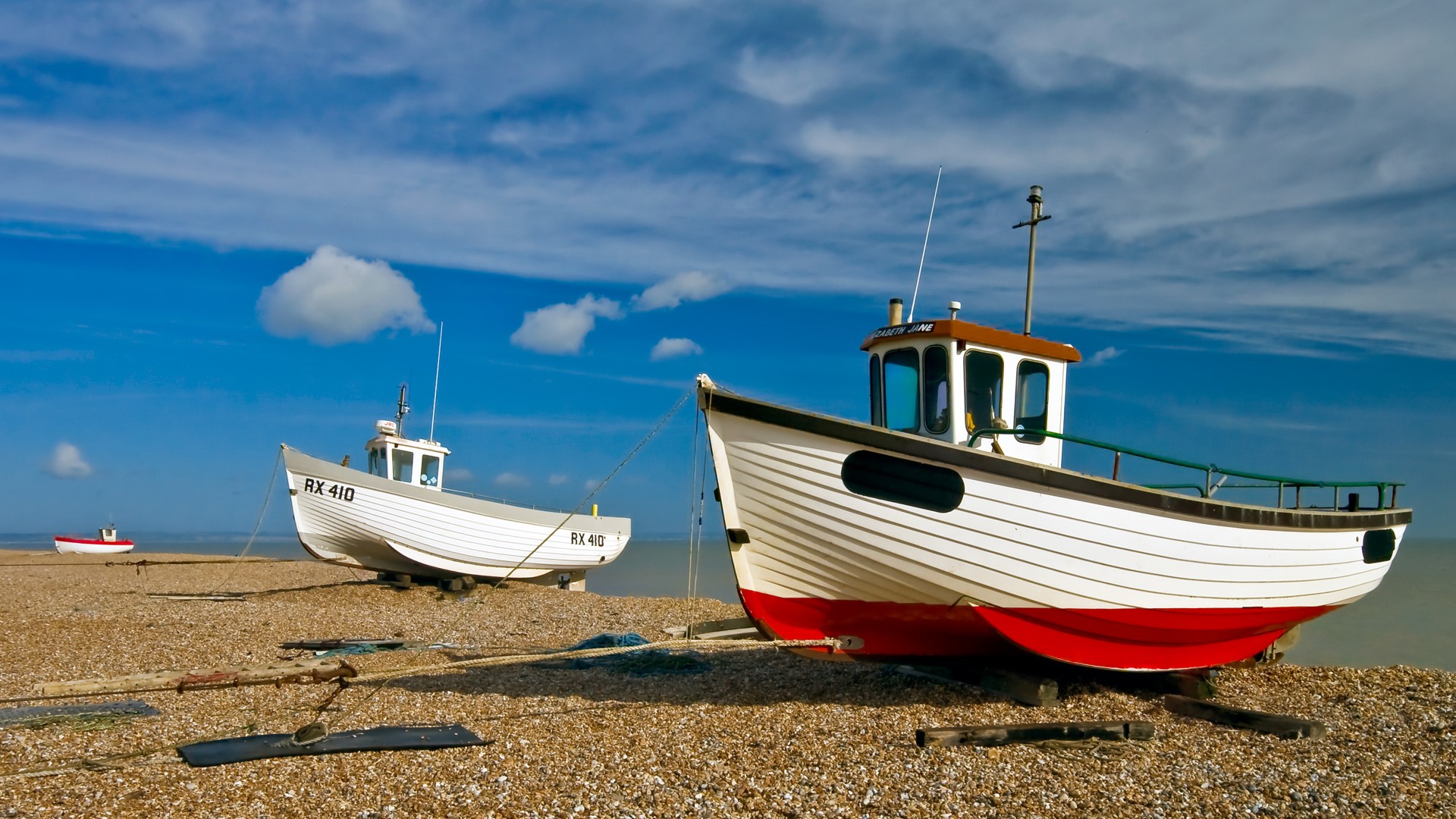 Fishing boats on a pebble beach under a blue sky HD Wallpaper