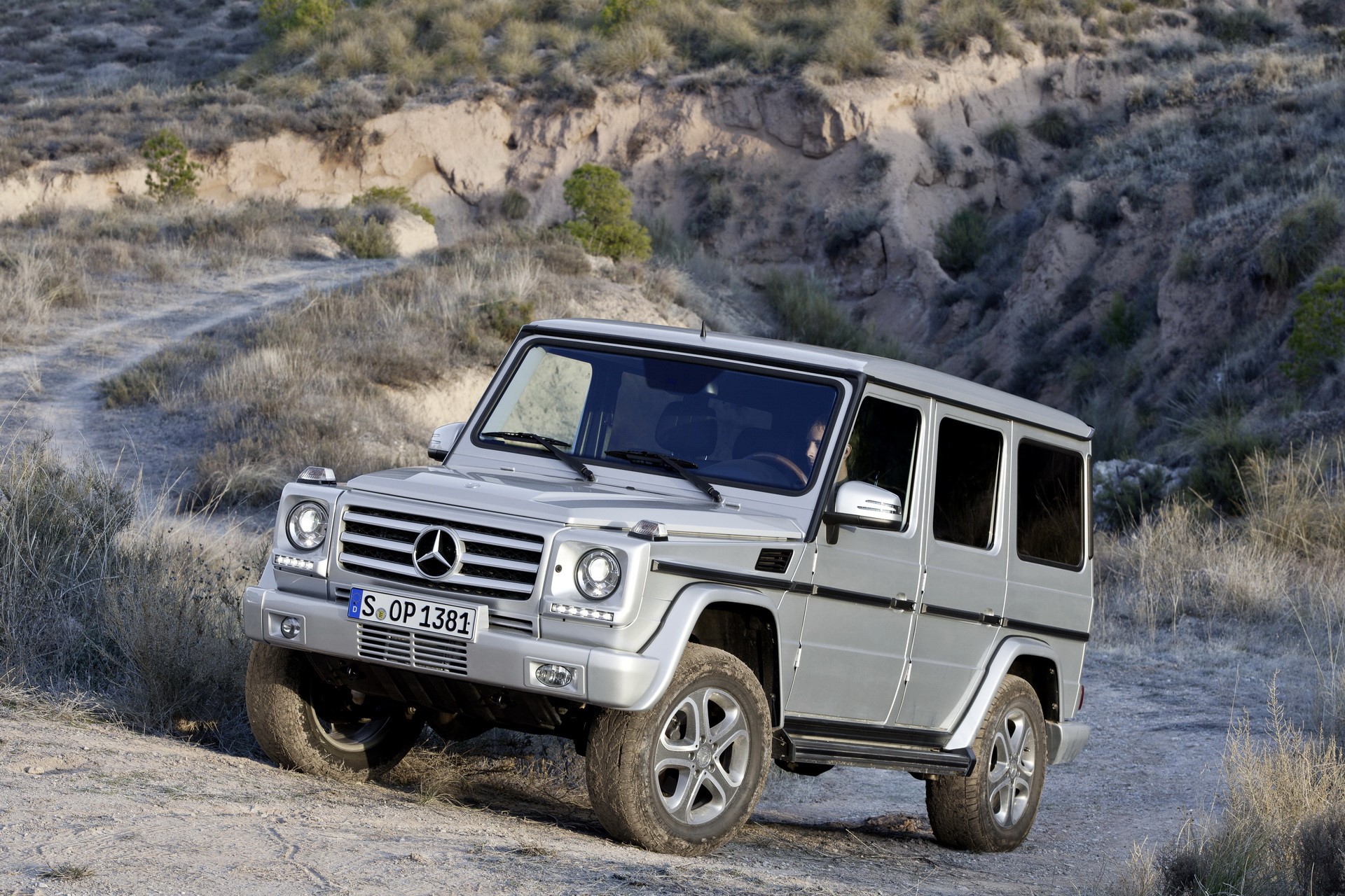 Silver Mercedes-Benz G-Class driving on a dirt road HD Wallpaper