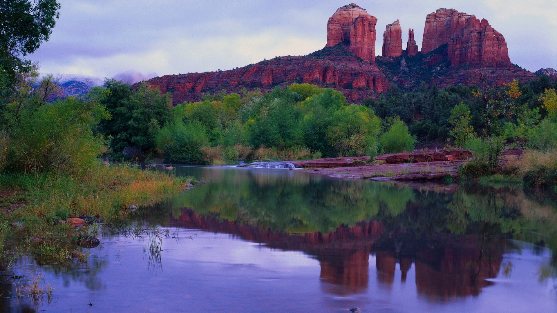 Red rock formations reflected in a calm river with trees HD Wallpaper