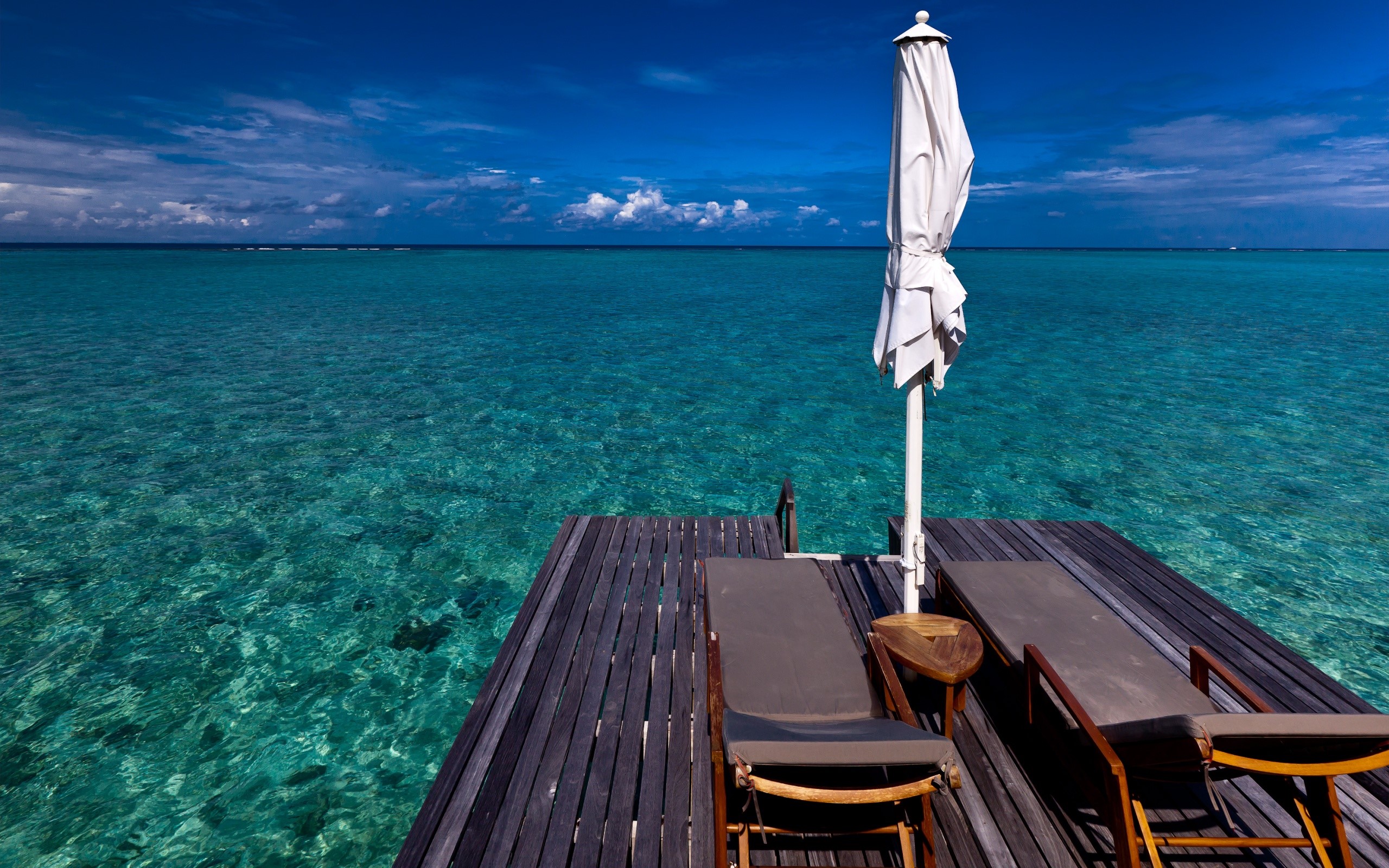 Wooden deck with lounge chairs and umbrella over turquoise water HD Wallpaper