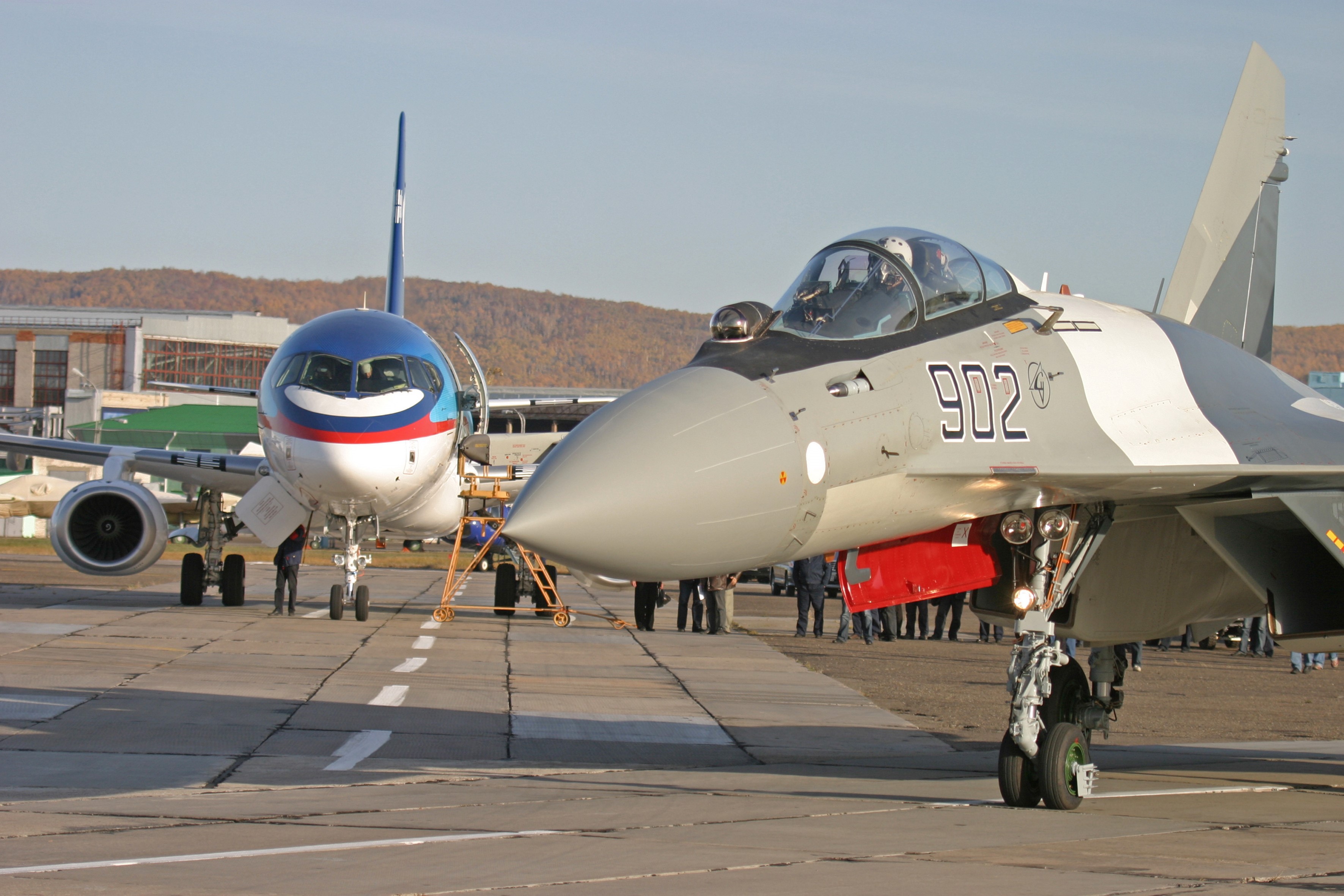 Sukhoi Su-35 fighter jet and passenger airplane on tarmac HD Wallpaper