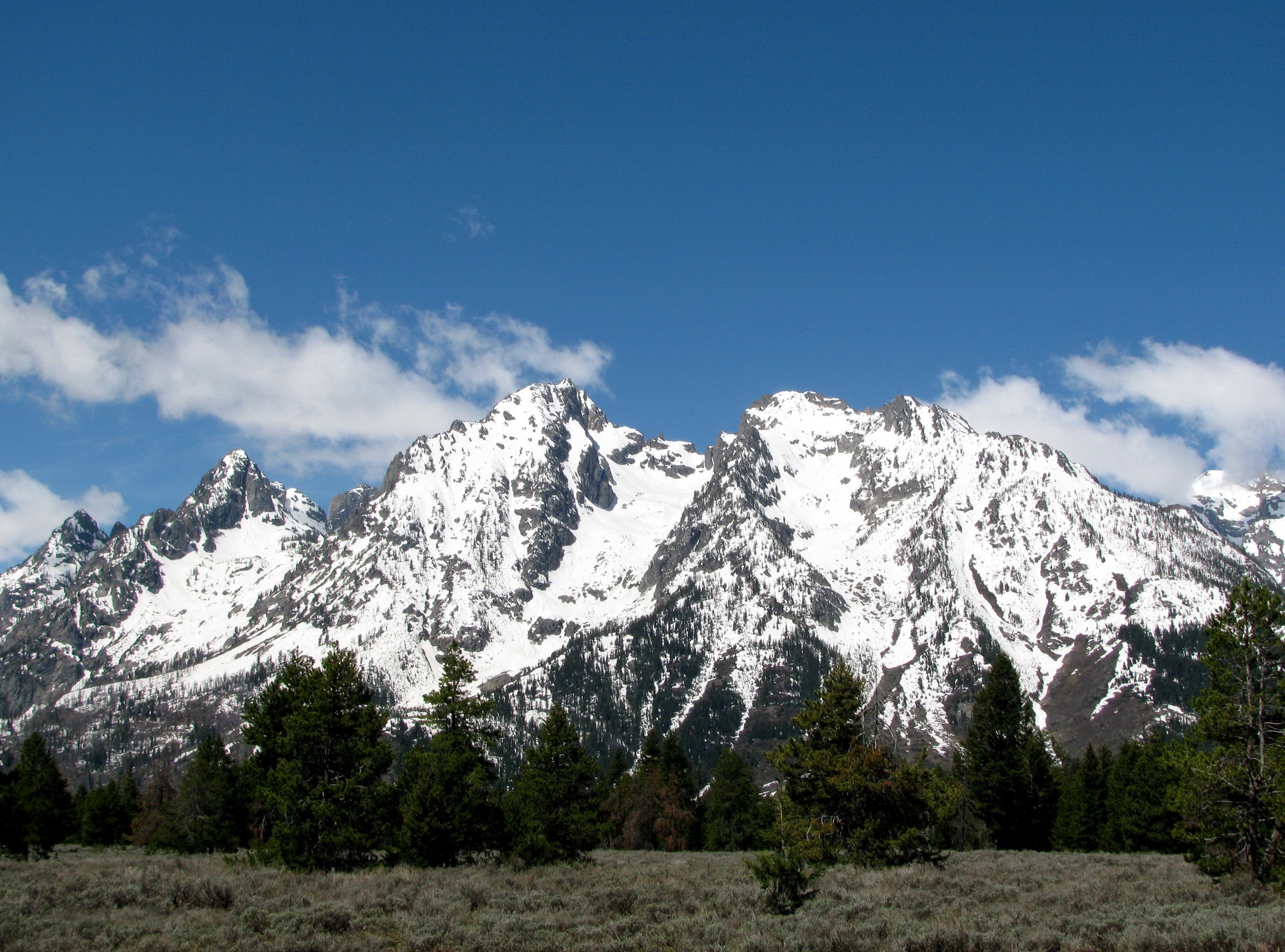 Snow-capped Grand Teton mountains in Wyoming under a blue sky HD Wallpaper