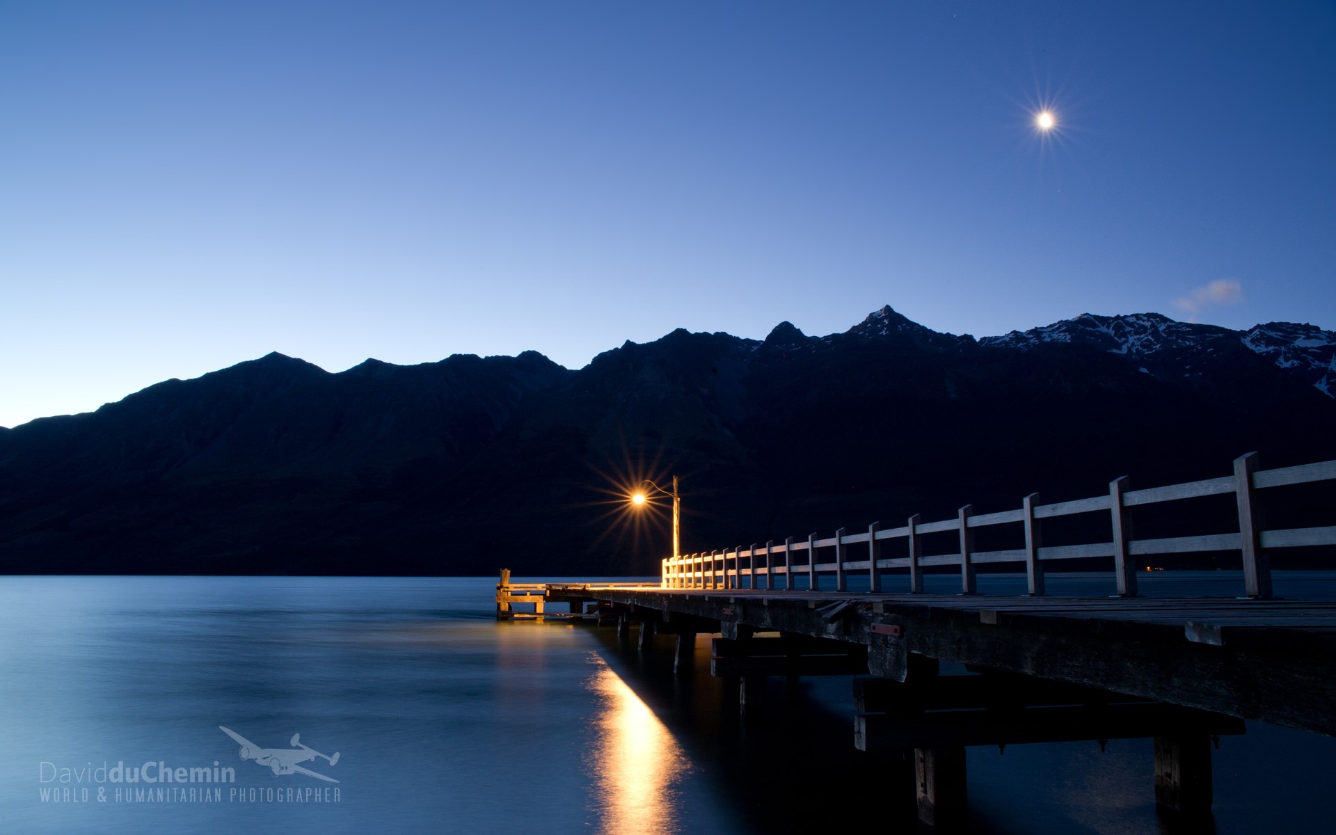 Wooden pier with a light at dusk near mountains HD Wallpaper