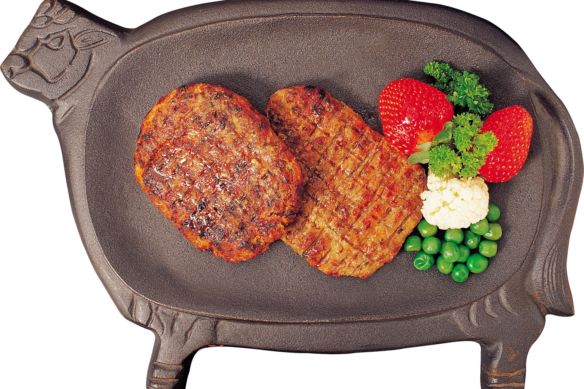 Two grilled patties on a pig-shaped cast iron platter with strawberries and peas HD Wallpaper