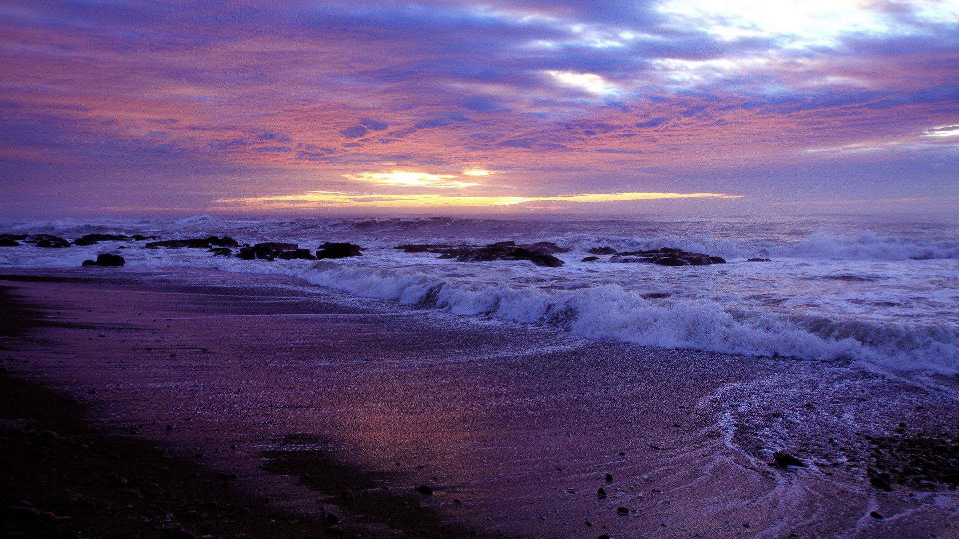 Purple sunset over a rocky beach with crashing waves HD Wallpaper