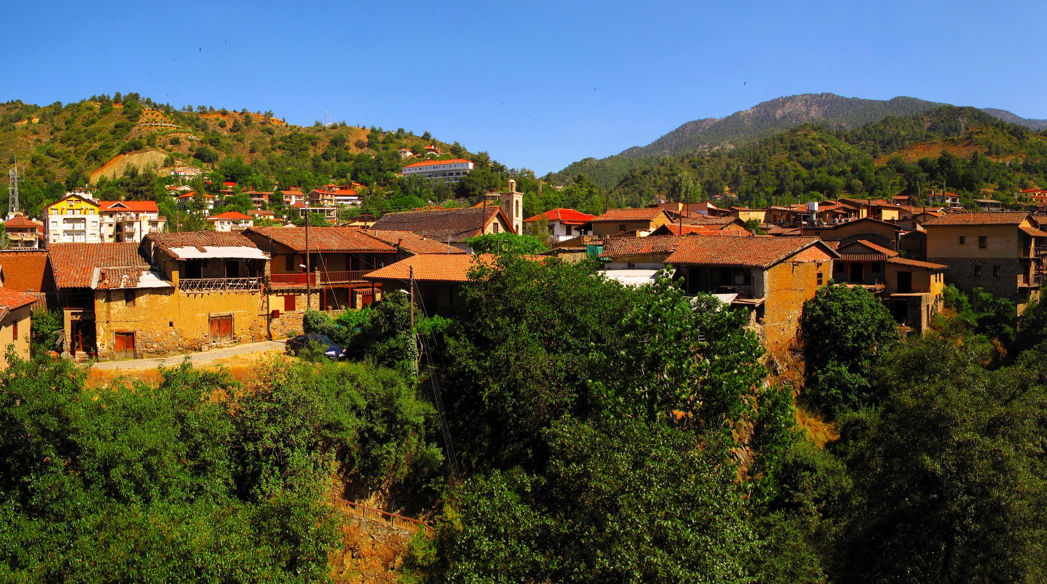 Traditional village with terracotta roofs and green hills HD Wallpaper