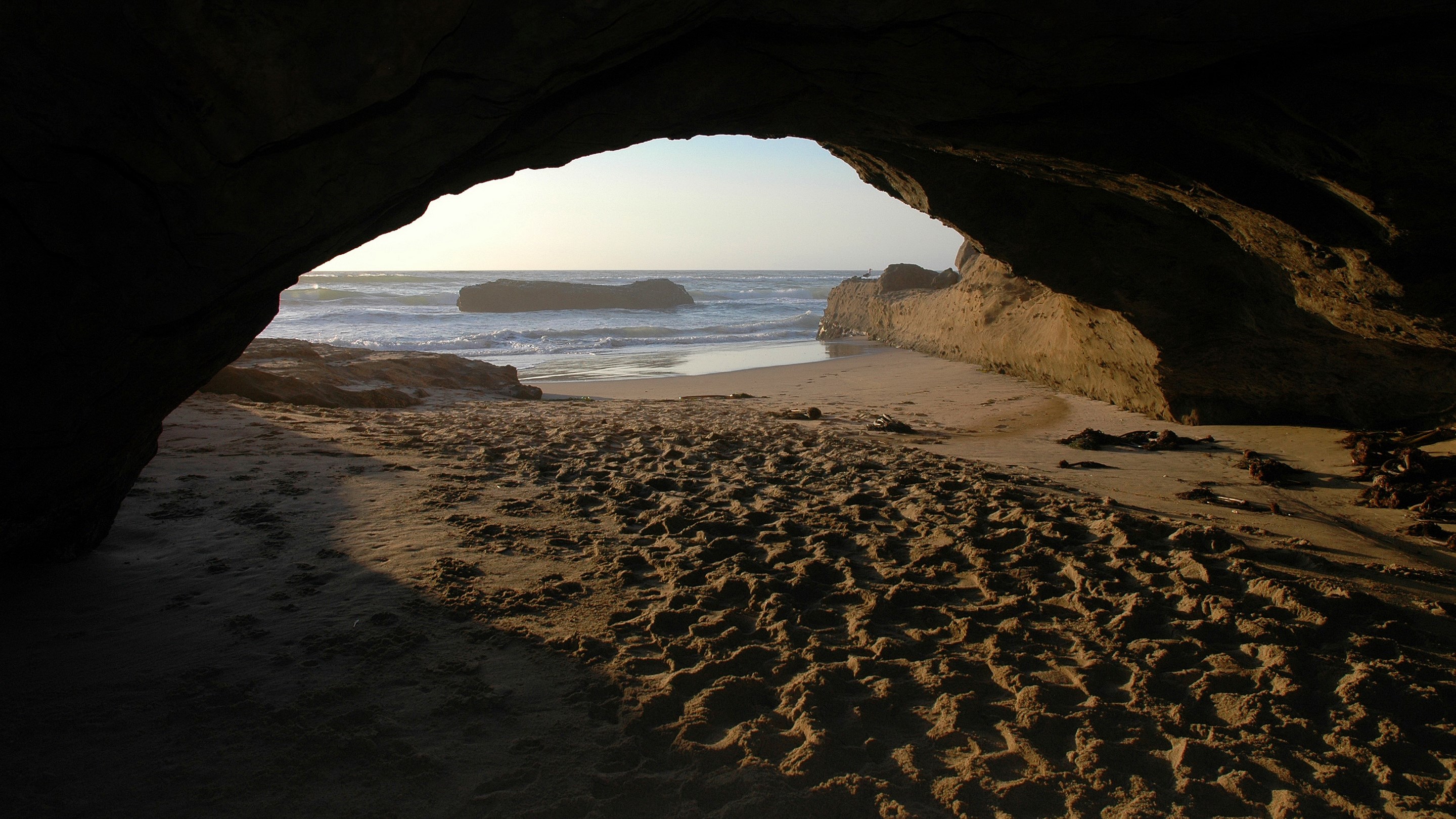 Cave entrance overlooking a beach and ocean HD Wallpaper