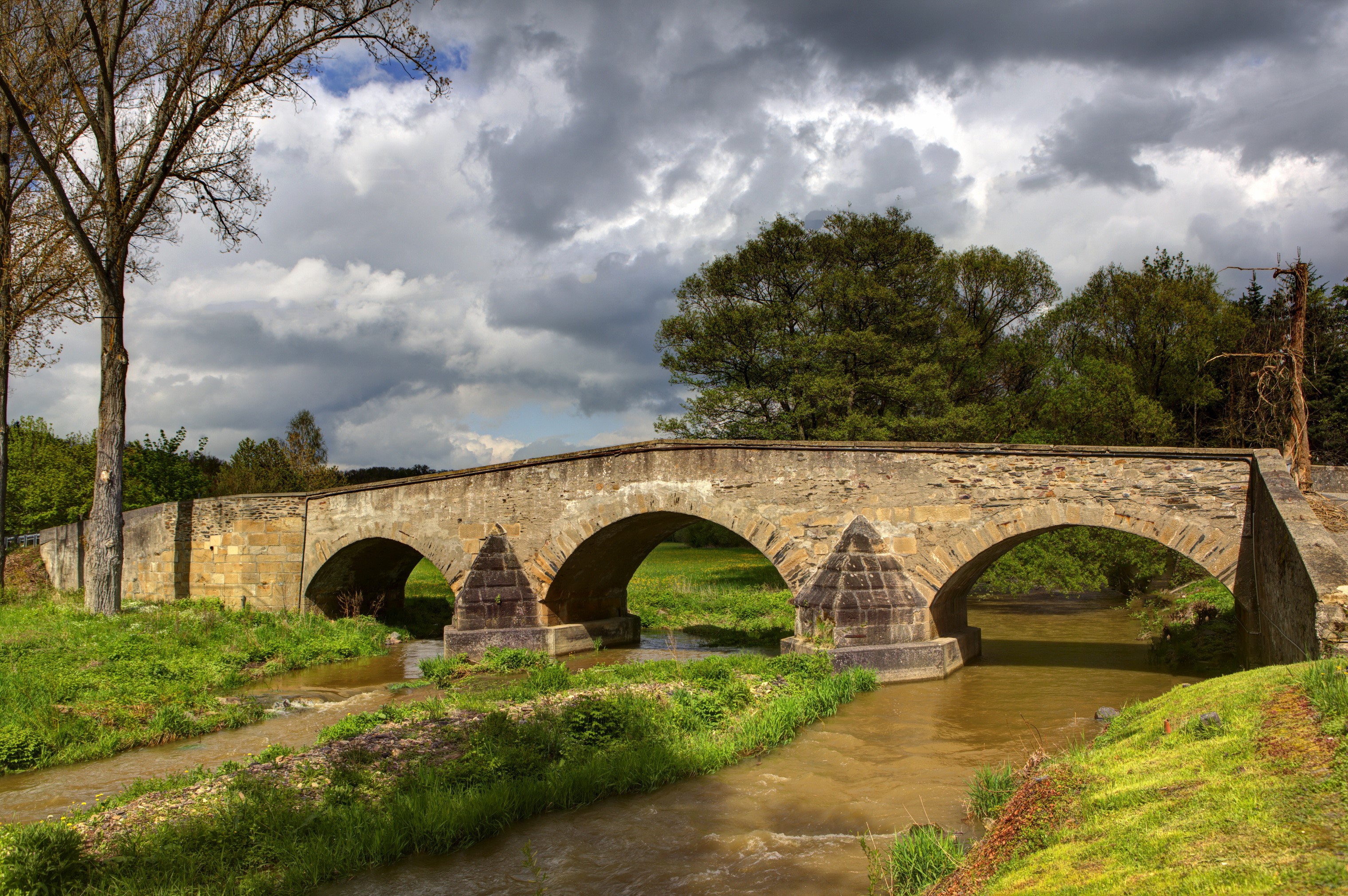 Stone arched bridge over a river with trees and clouds HD Wallpaper