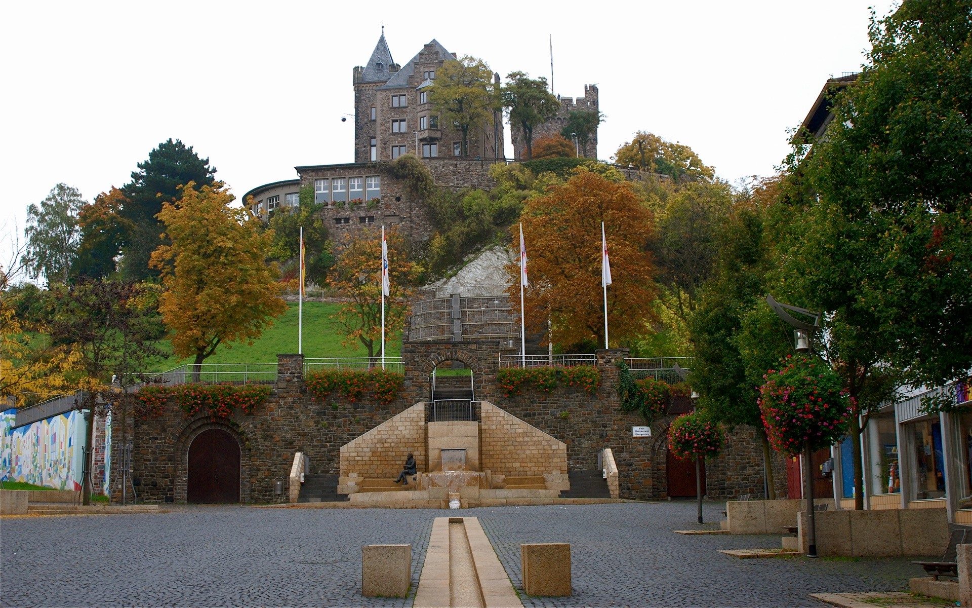 Castle on a hill with autumn trees and a town square HD Wallpaper