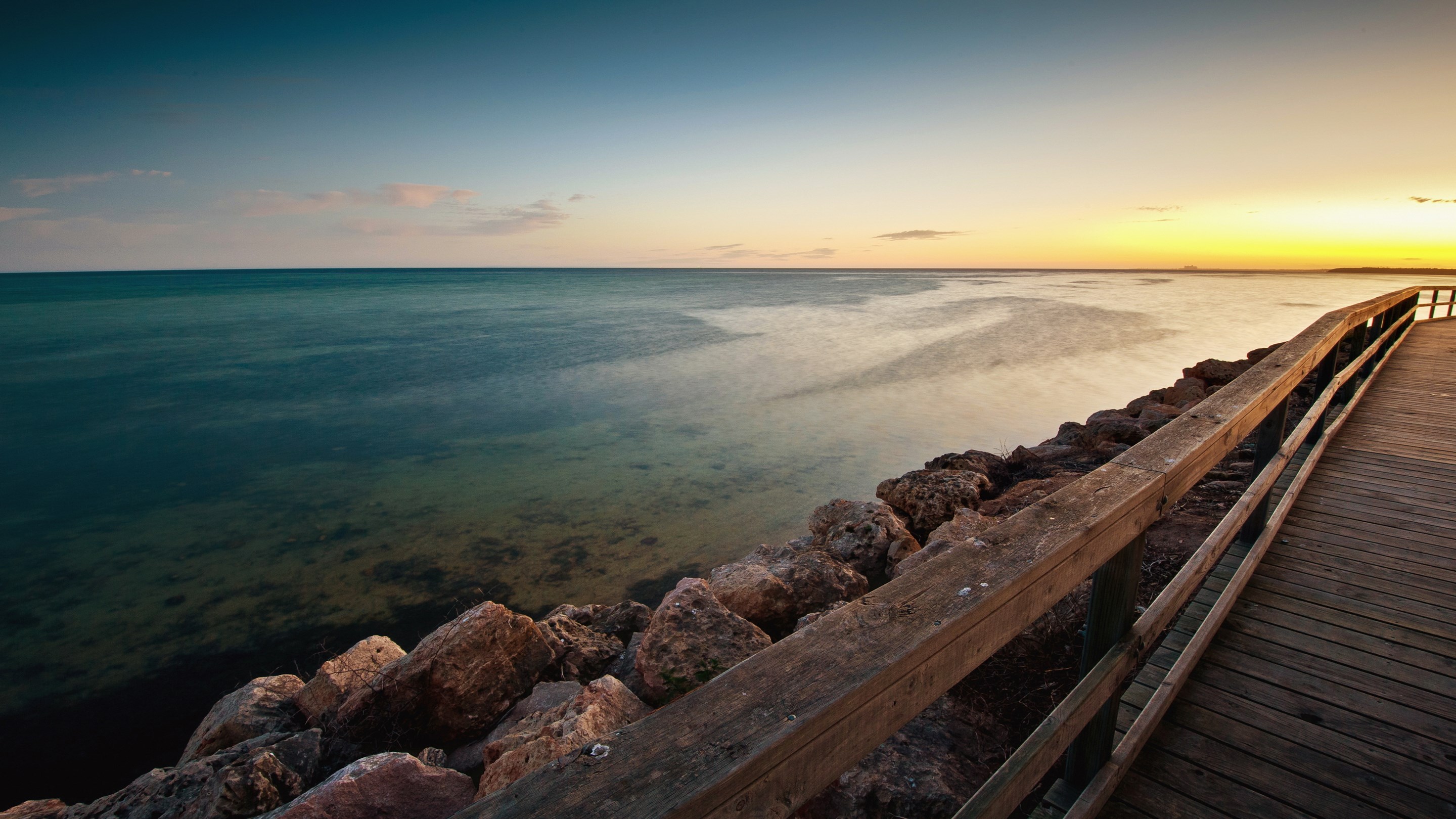 Wooden pier and rocky shore at sunset HD Wallpaper