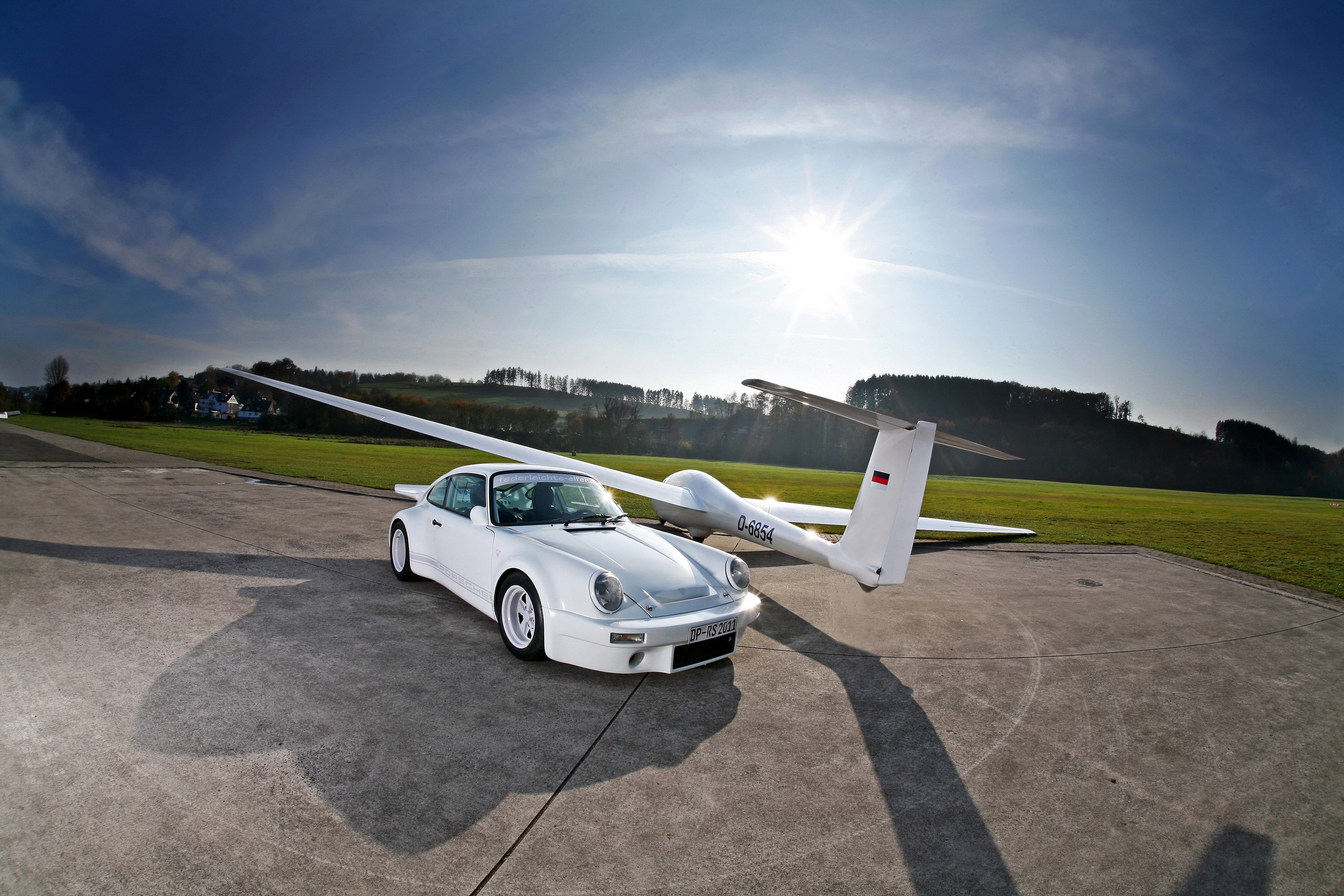 White Porsche 911 next to a glider on an airfield HD Wallpaper