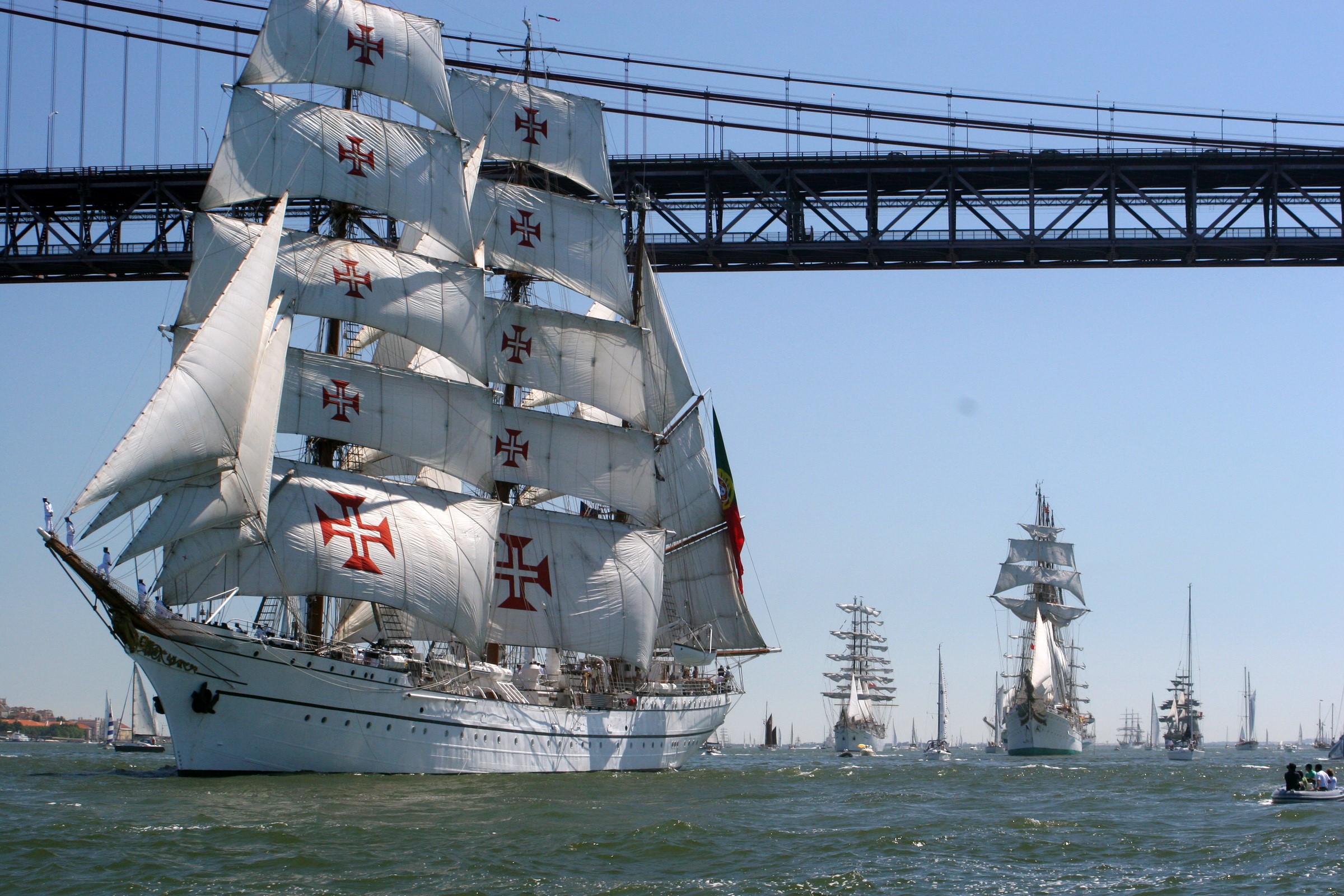 Tall ships with Portuguese flags under a bridge HD Wallpaper