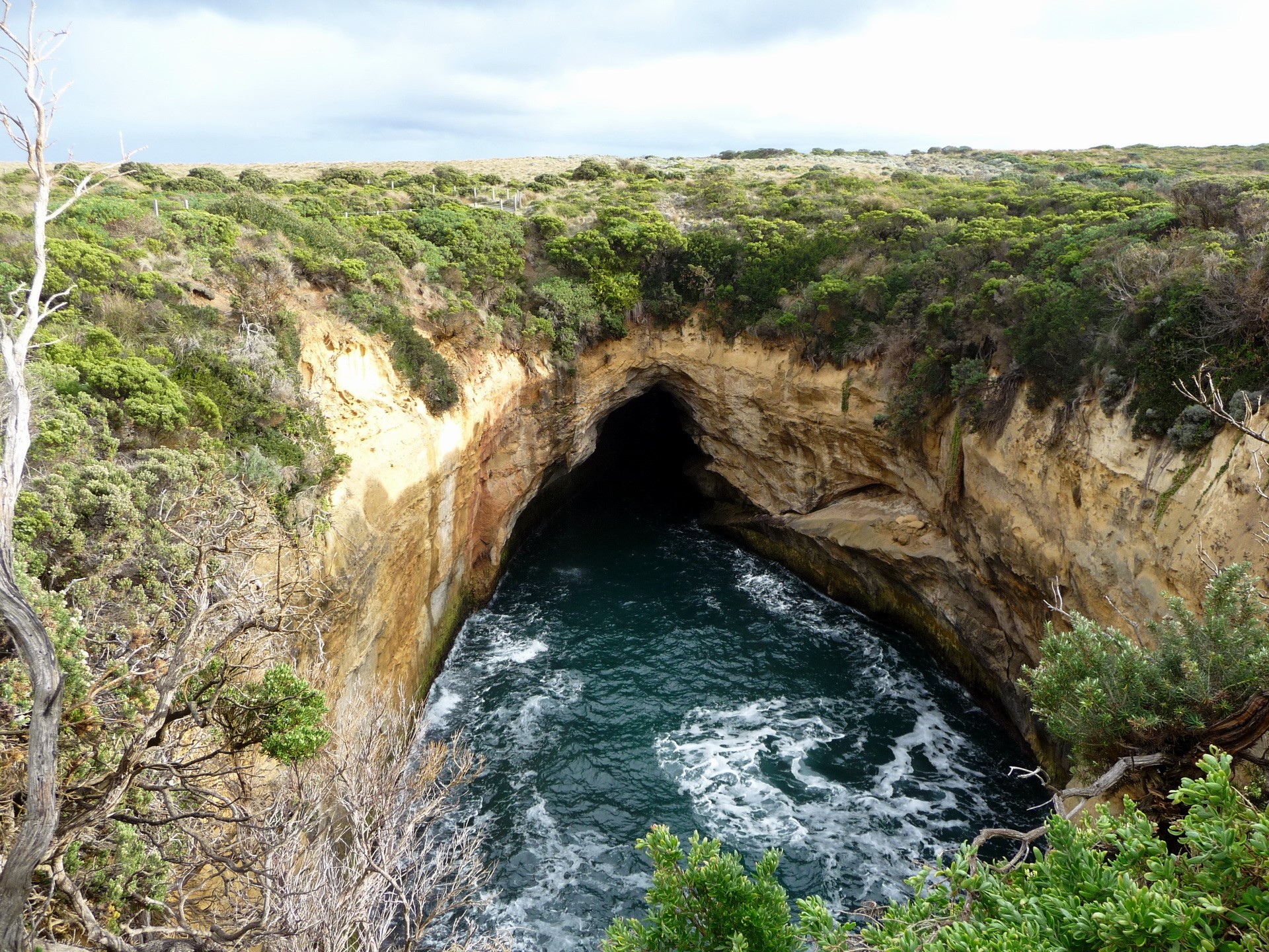 Cave entrance in a cliff face with ocean waves HD Wallpaper