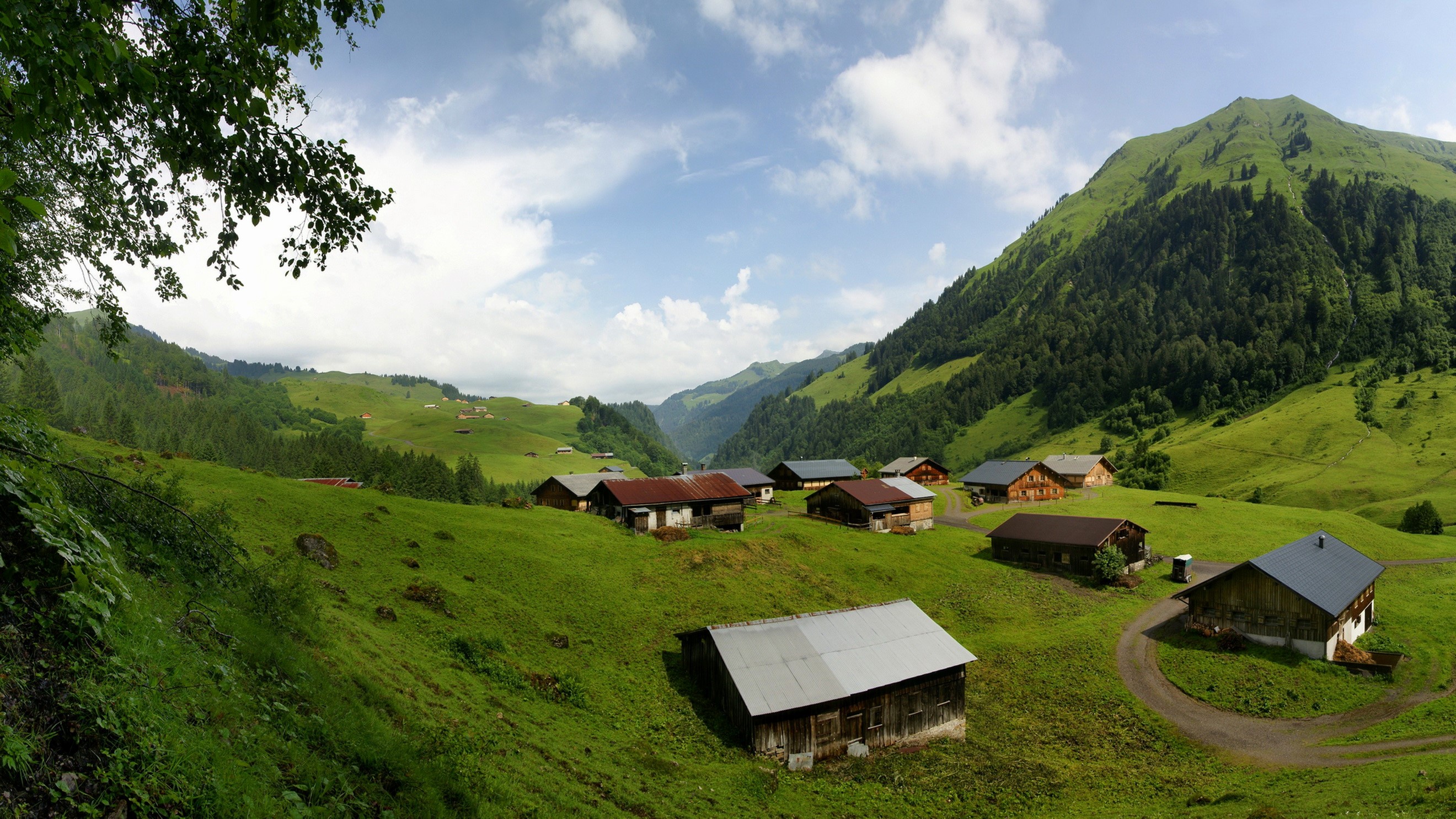 Alpine village with green mountains and clouds HD Wallpaper