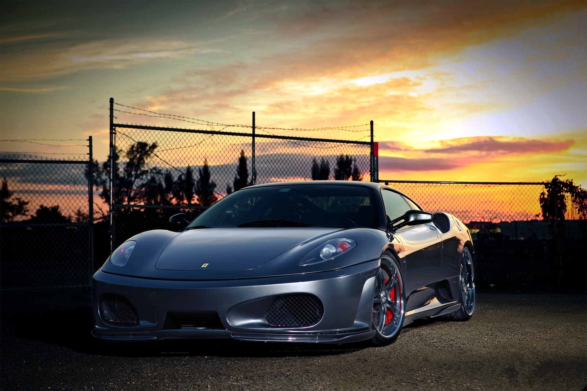 Gray Ferrari F430 parked near a fence at sunset HD Wallpaper