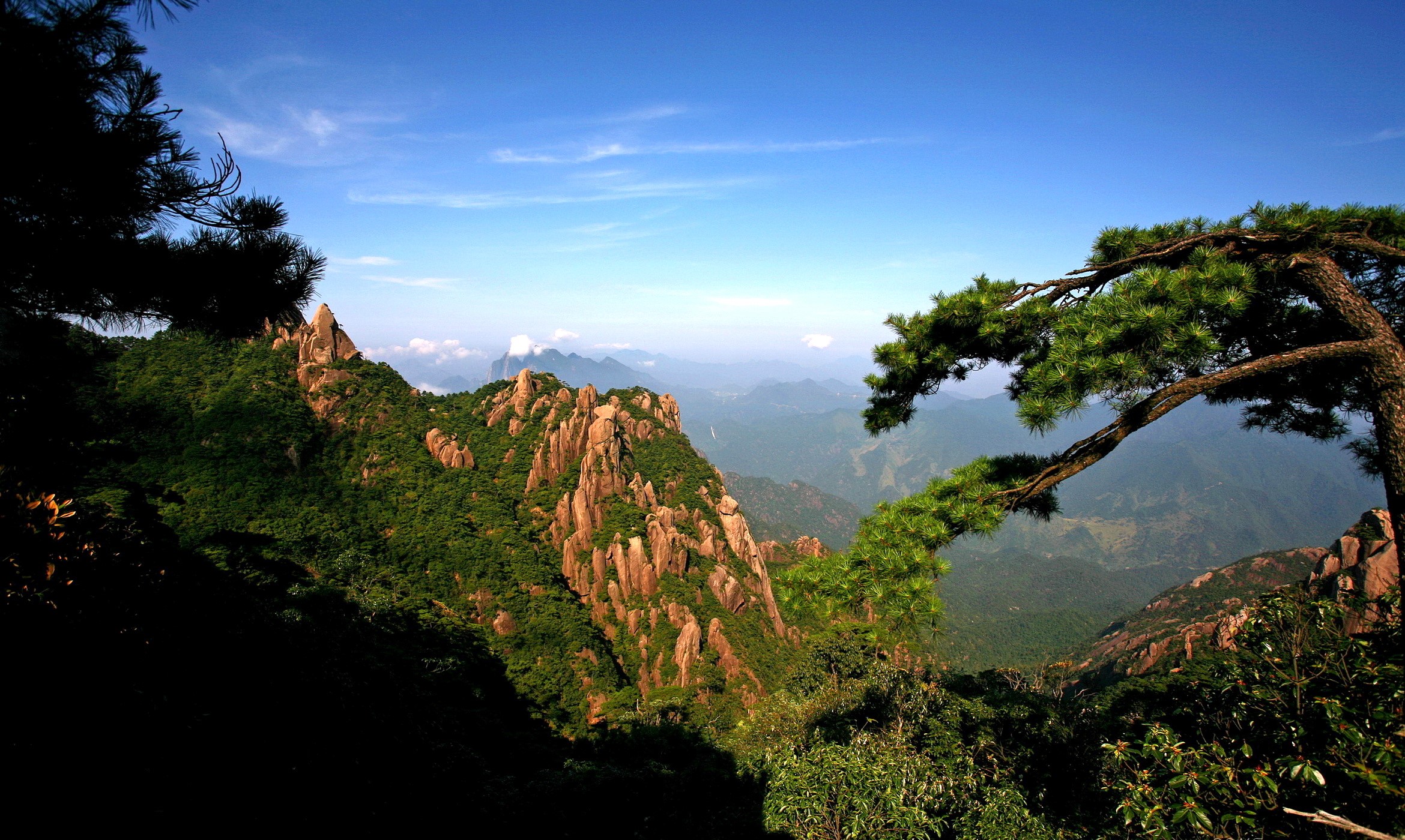 Jagged mountains covered in green trees under a blue sky HD Wallpaper