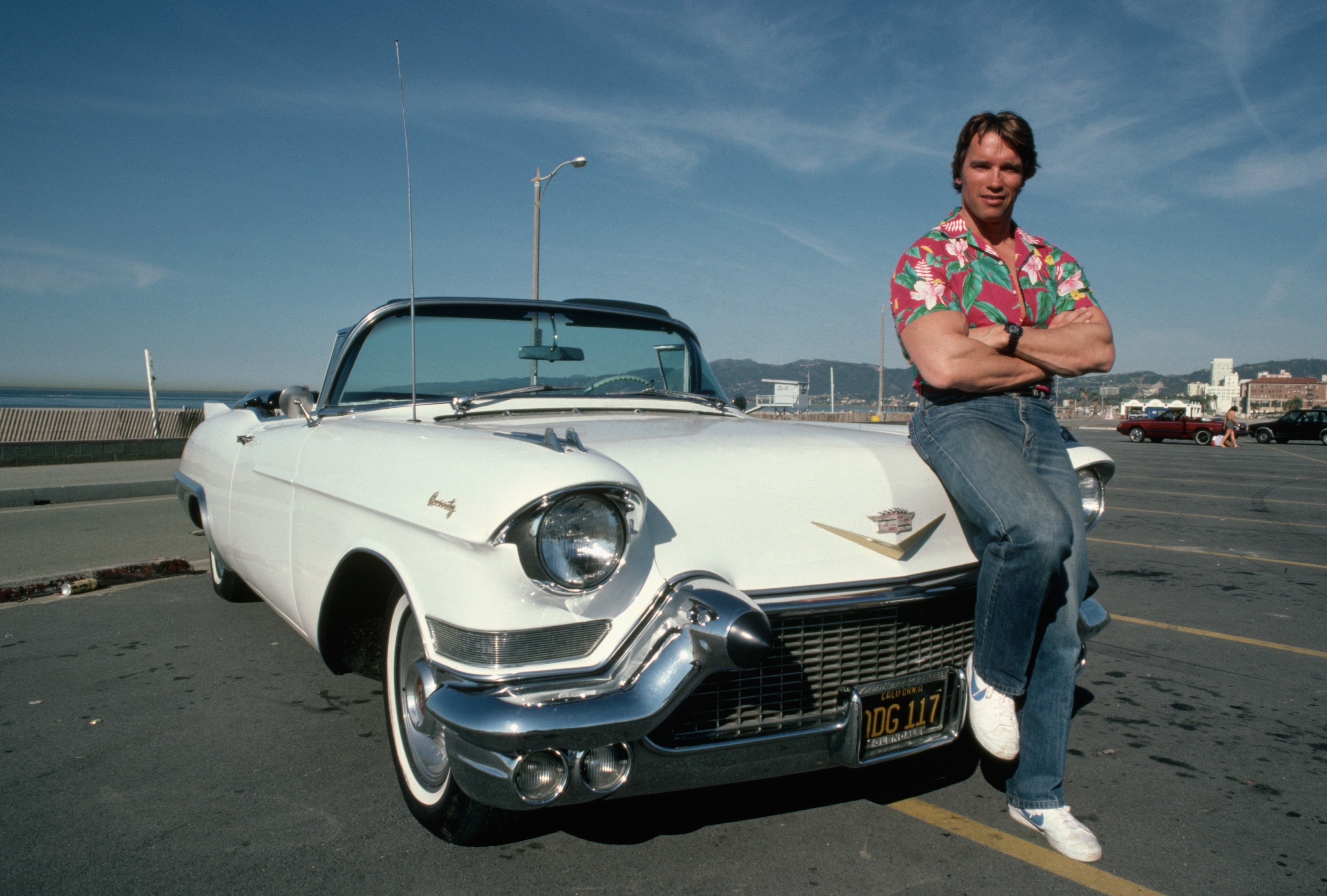 Arnold Schwarzenegger leaning on a white Cadillac convertible HD Wallpaper