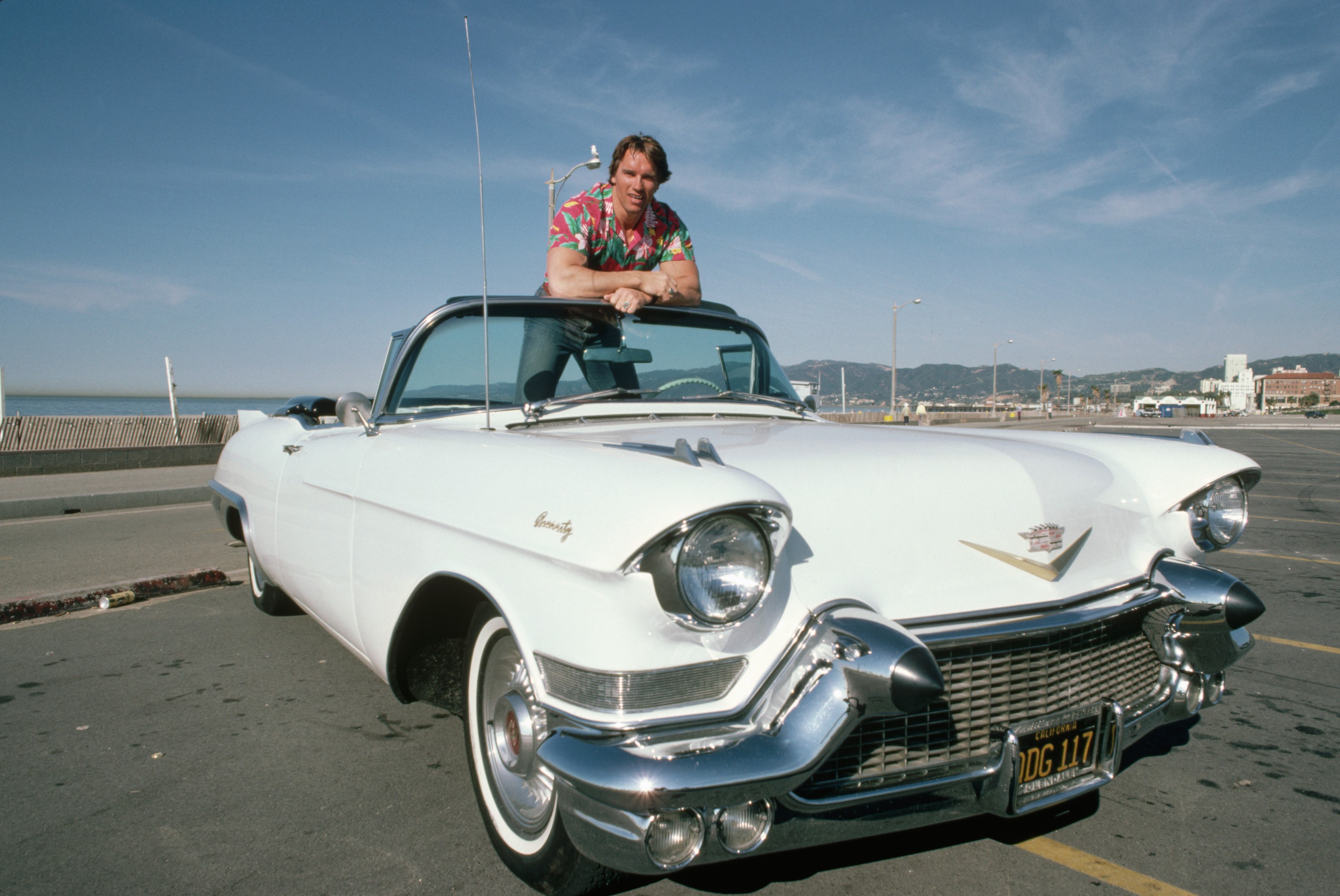 Arnold Schwarzenegger with a white 1950s Cadillac convertible HD Wallpaper