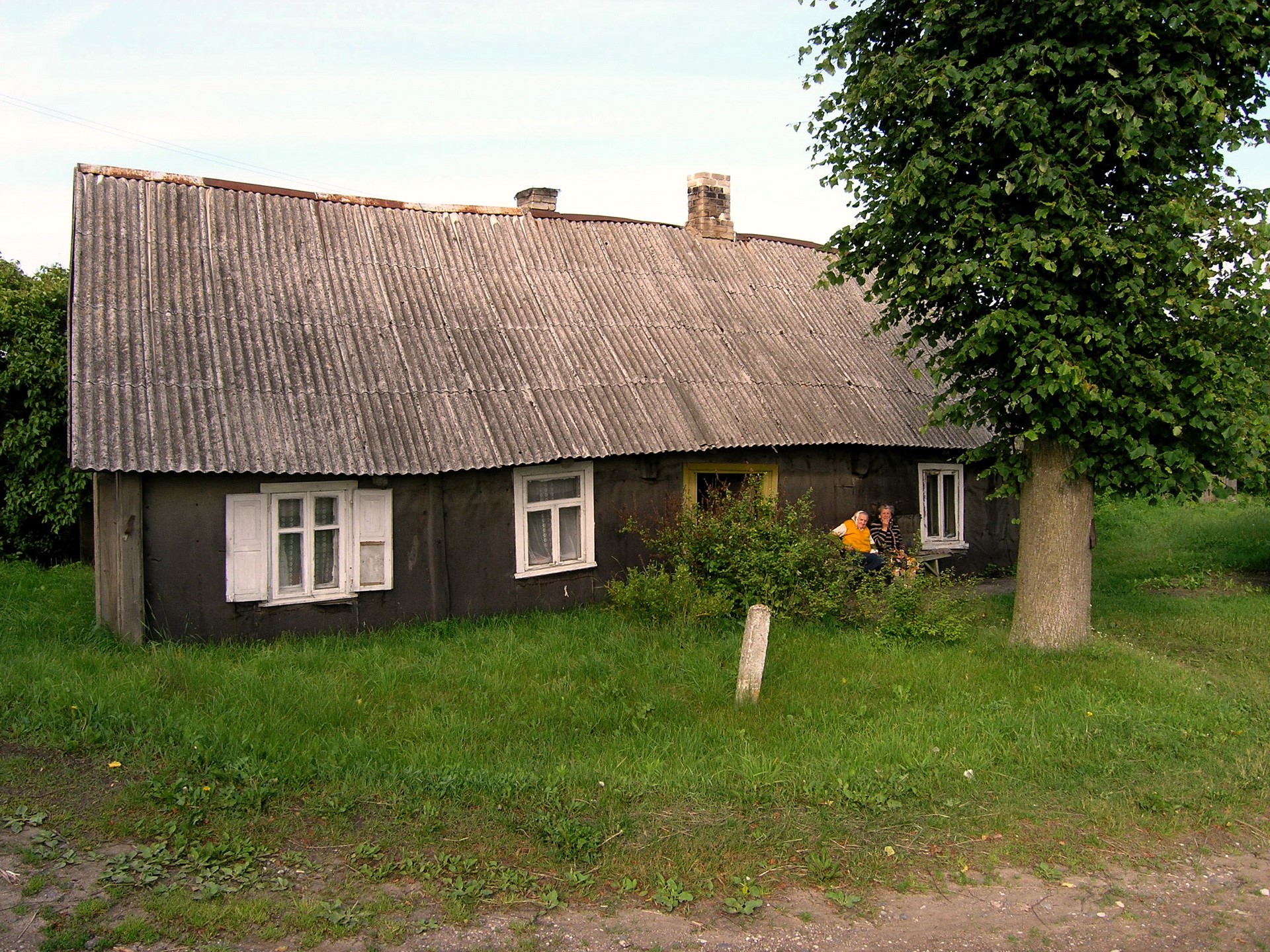 Two people sitting on a bench outside a rustic house HD Wallpaper