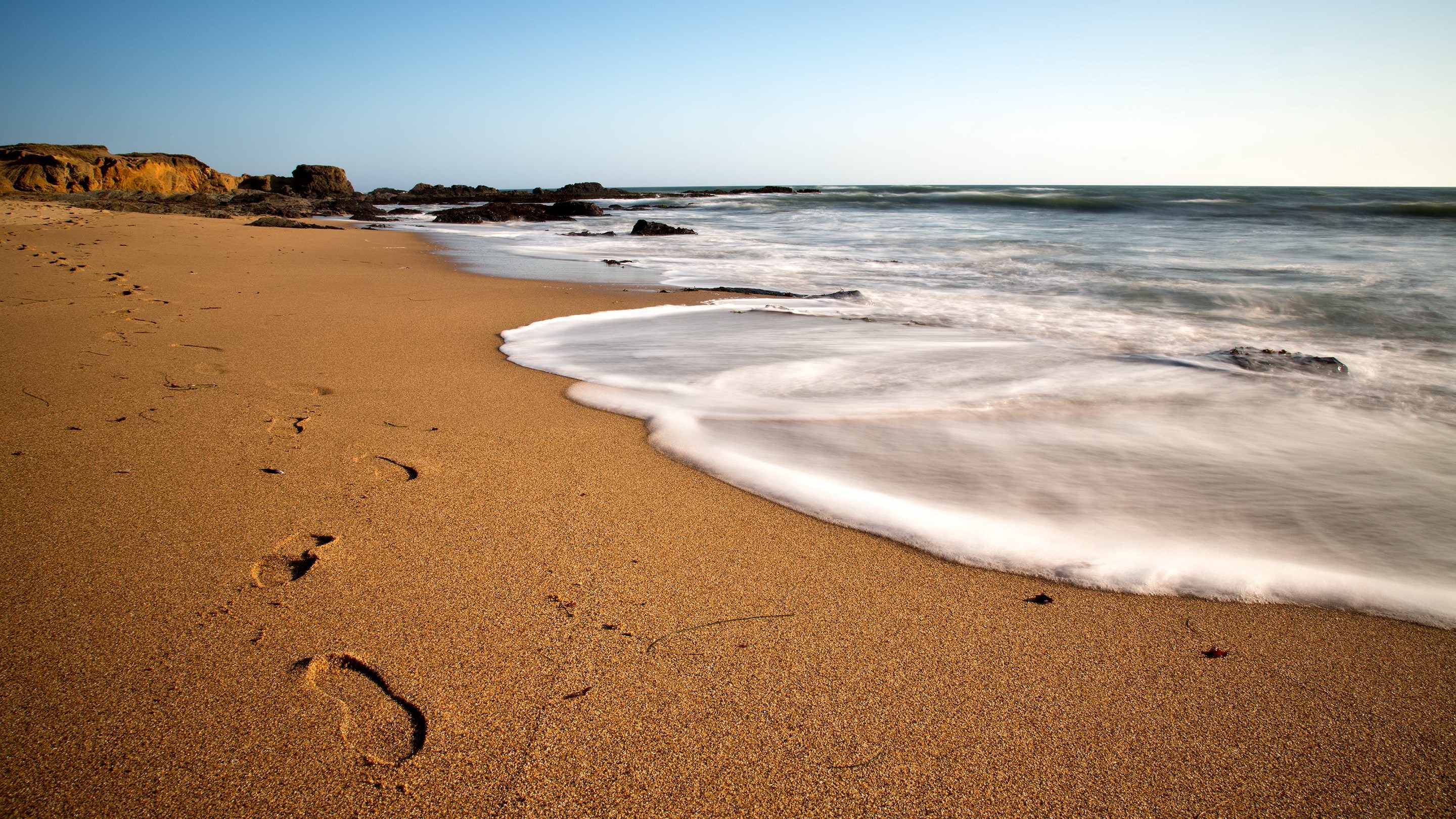 Footprints on a sandy beach with waves HD Wallpaper